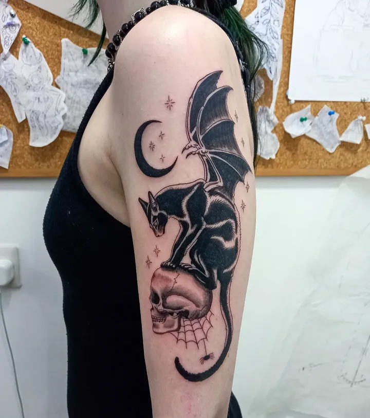 Bat-winged cat on skull with moon upper arm tattoo by Tori Talio