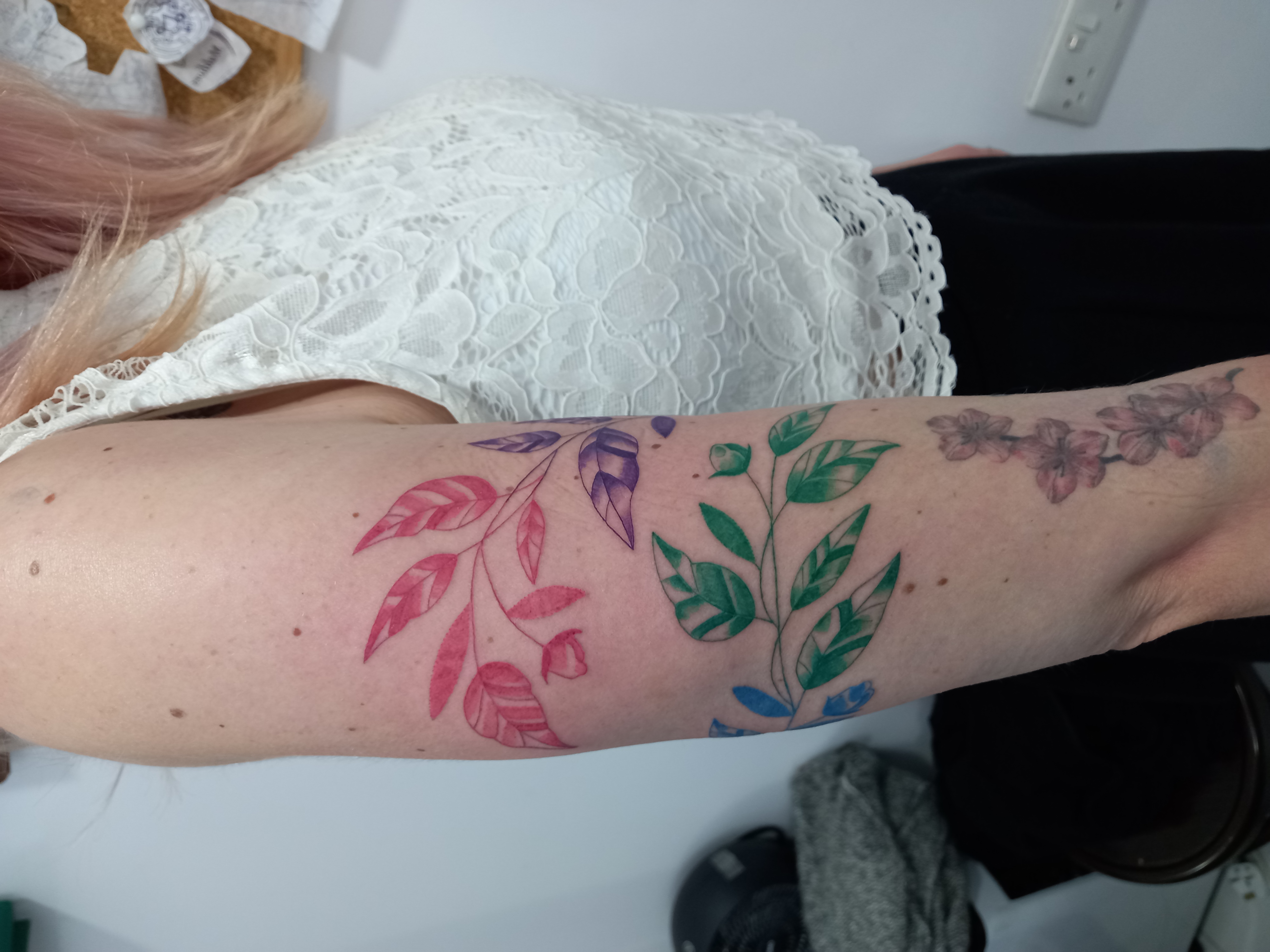 Colourful botanical leaves red green purple upper arm tattoo by Tori Talio