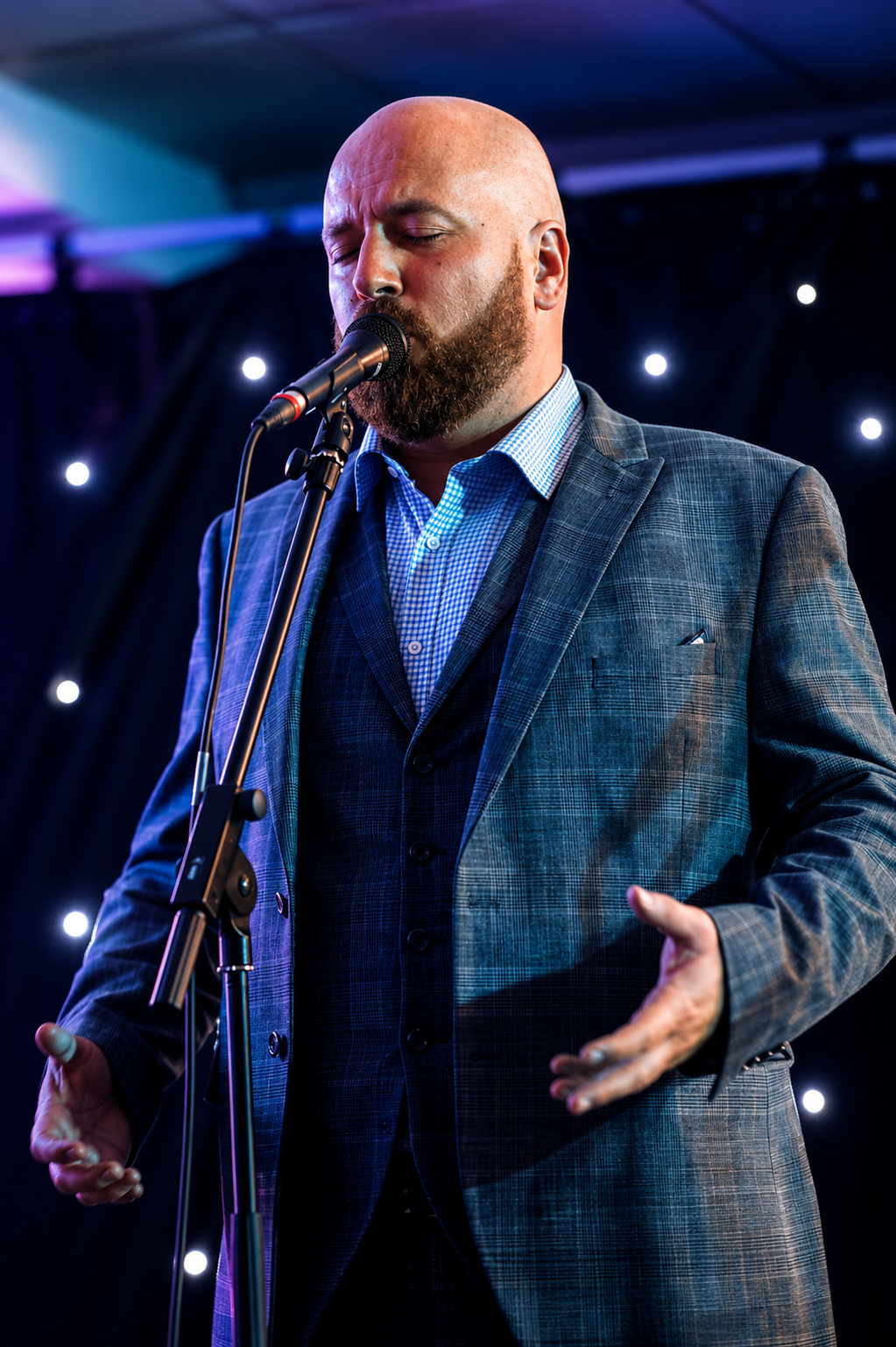 Ryan Wallace — The Opera Guy singing on stage in a checked suit with starlight backdrop