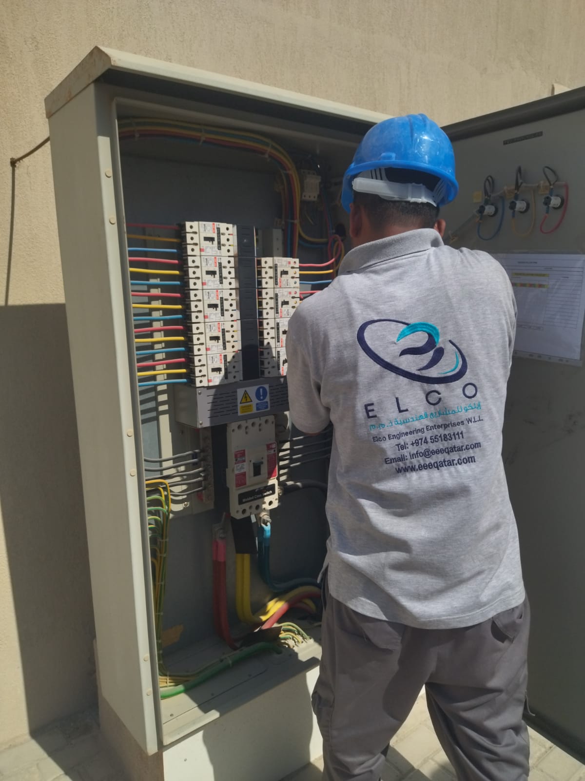 ELCO technician in branded shirt and blue helmet working on electrical distribution panel with color-coded wiring