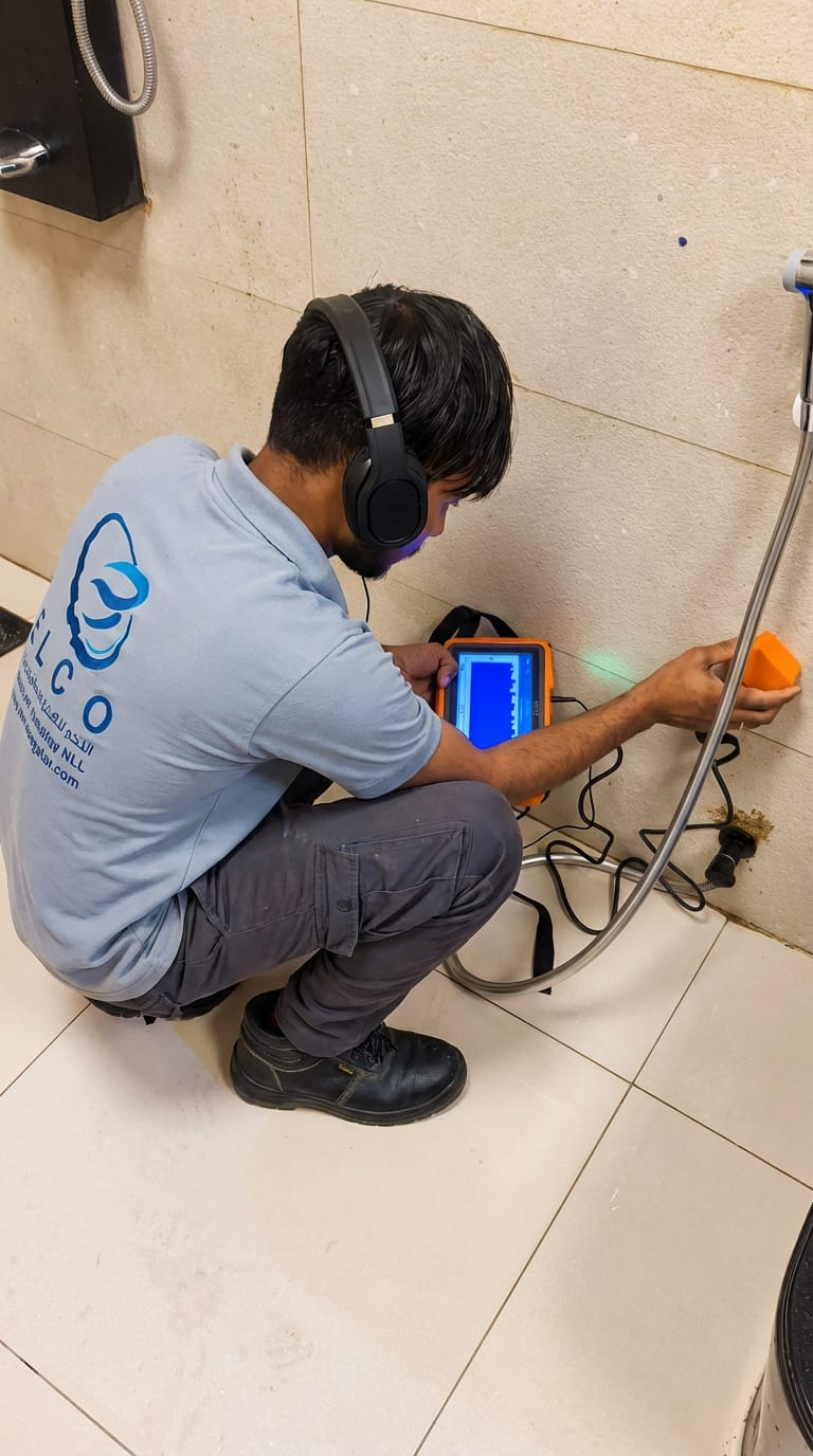 ELCO technician in branded shirt using electronic acoustic leak detection equipment with headphones and digital scanner