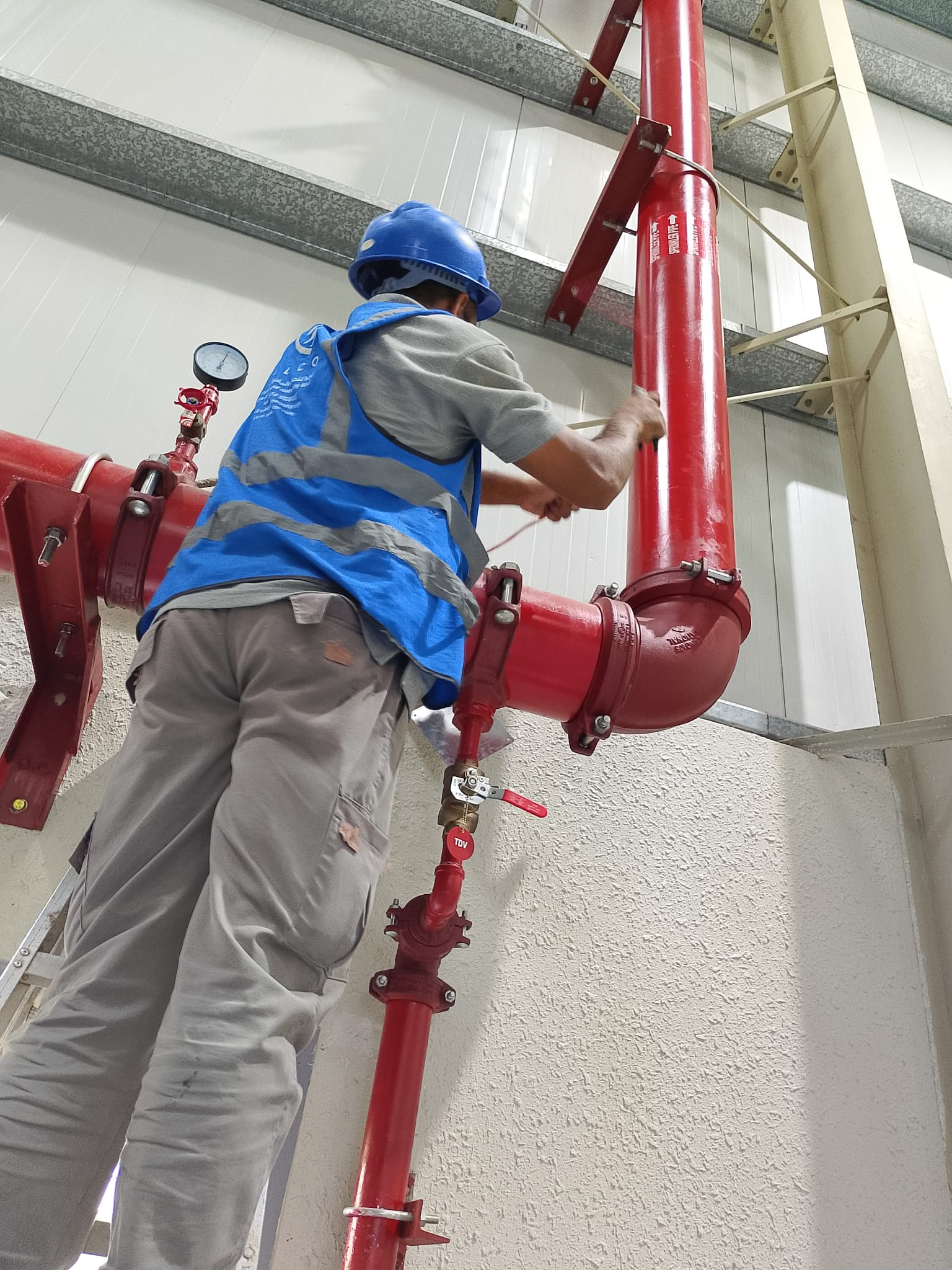 ELCO worker in branded blue vest and helmet installing red fire fighting piping and valve system