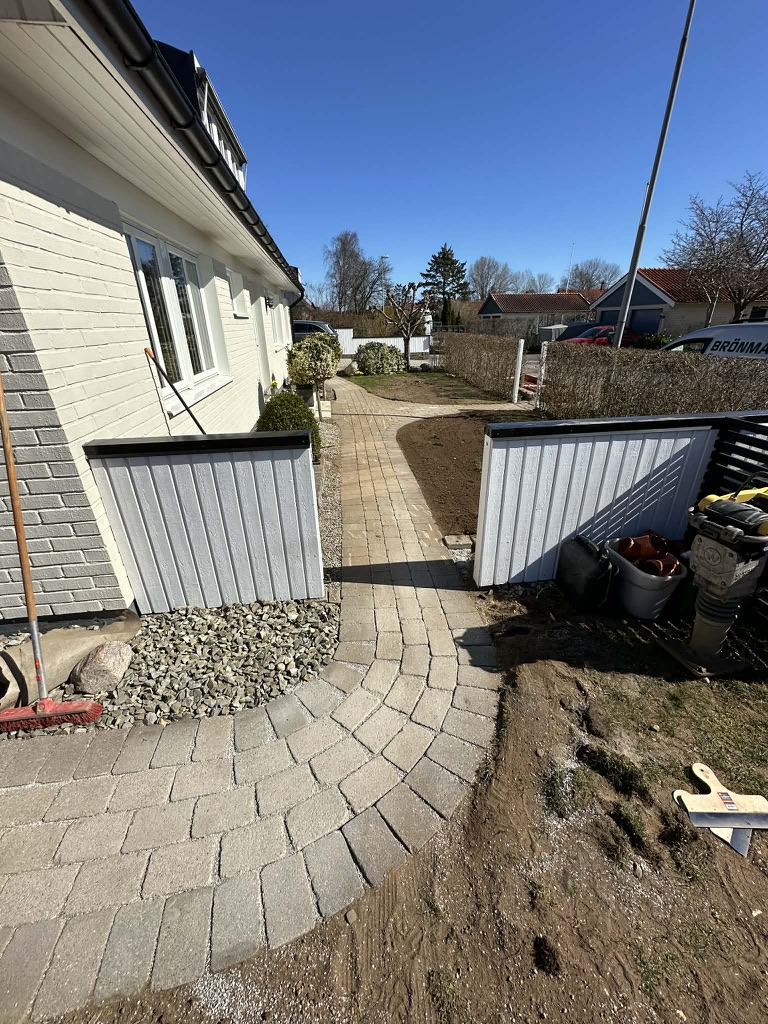 Stensättning av gångväg längs fasad med marksten och kantsten
