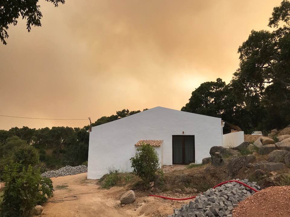 The farmhouse under smoke, with the fire approaching from the ridge above