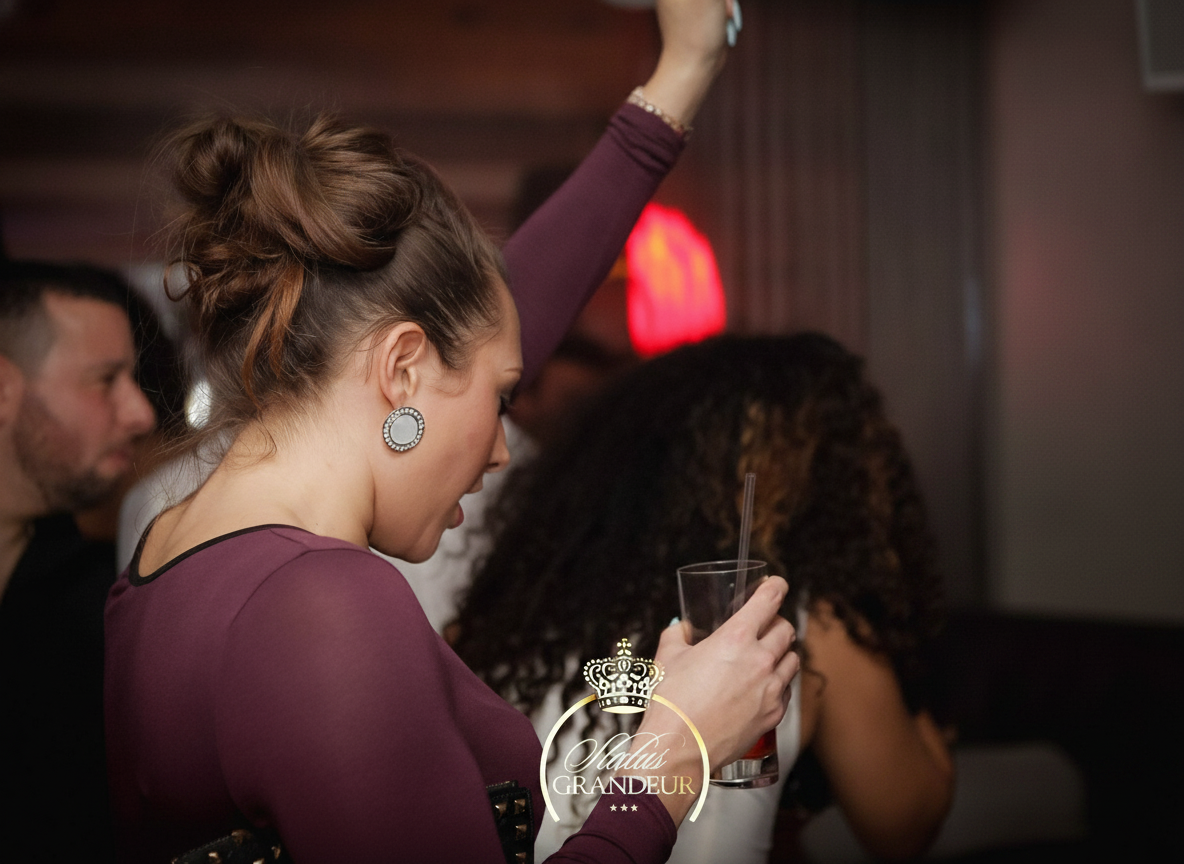 Status Grandeur event — woman in burgundy top dancing with drink raised