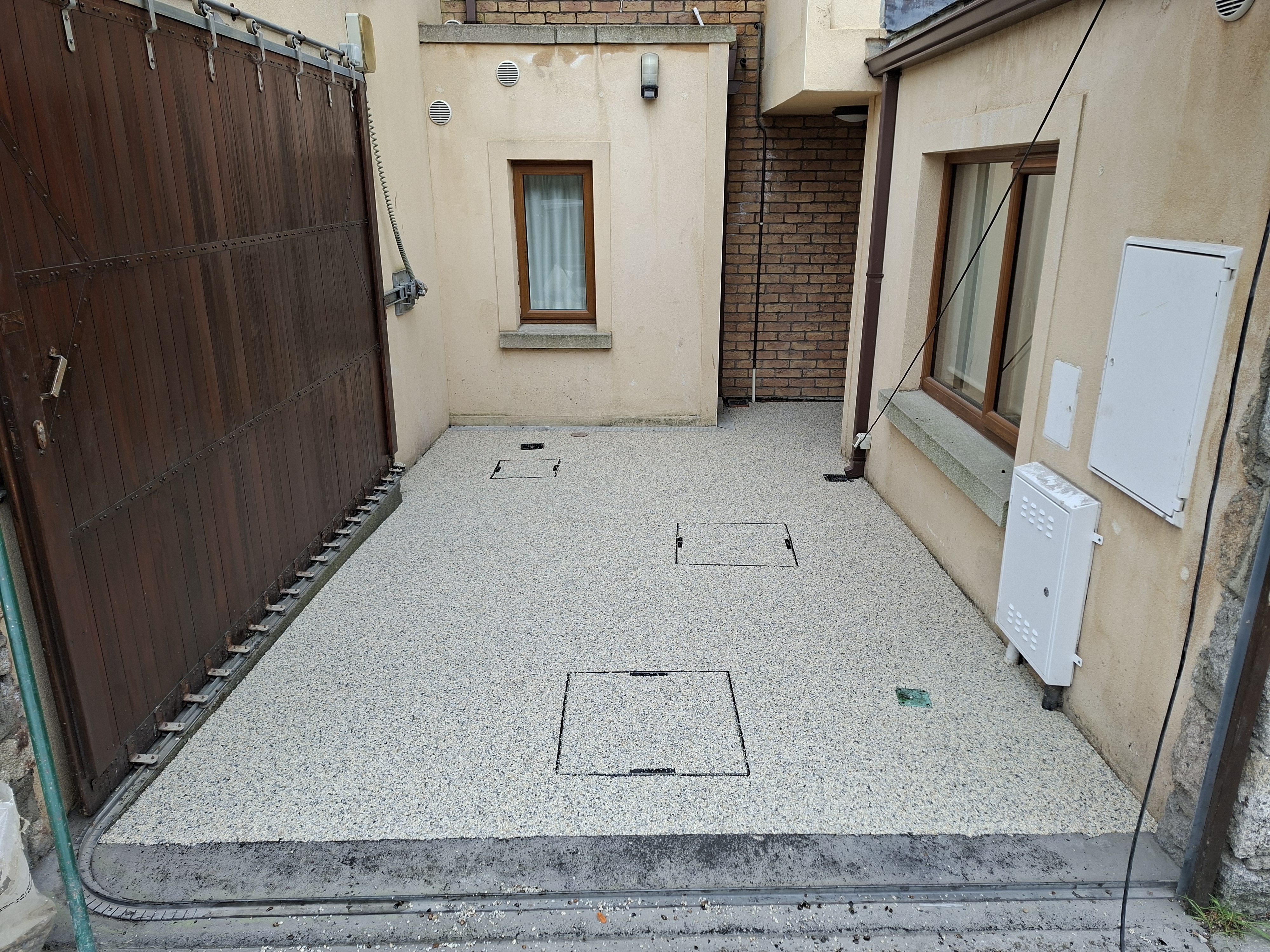 Light grey resin bound courtyard surface with tidy edges and access covers, low-maintenance finish