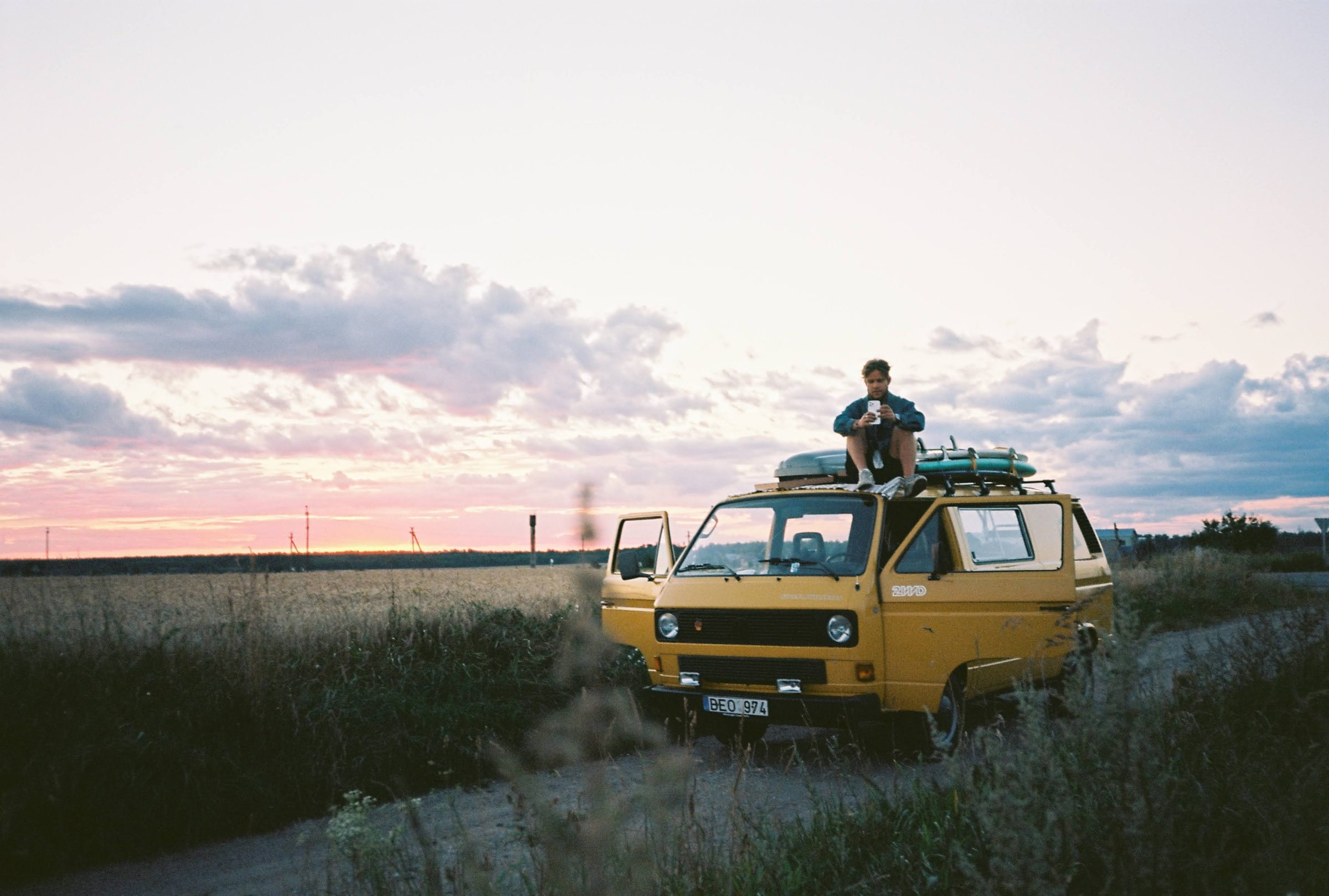 A yellow Birbi Volkswagen T3 van parked in a field at sunset