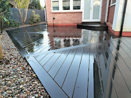 Wide shot dark composite decking wrapping around brick building by Woodgate Joinery Glasgow