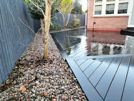 Dark composite decking with pebble border and tree by Woodgate Joinery Glasgow