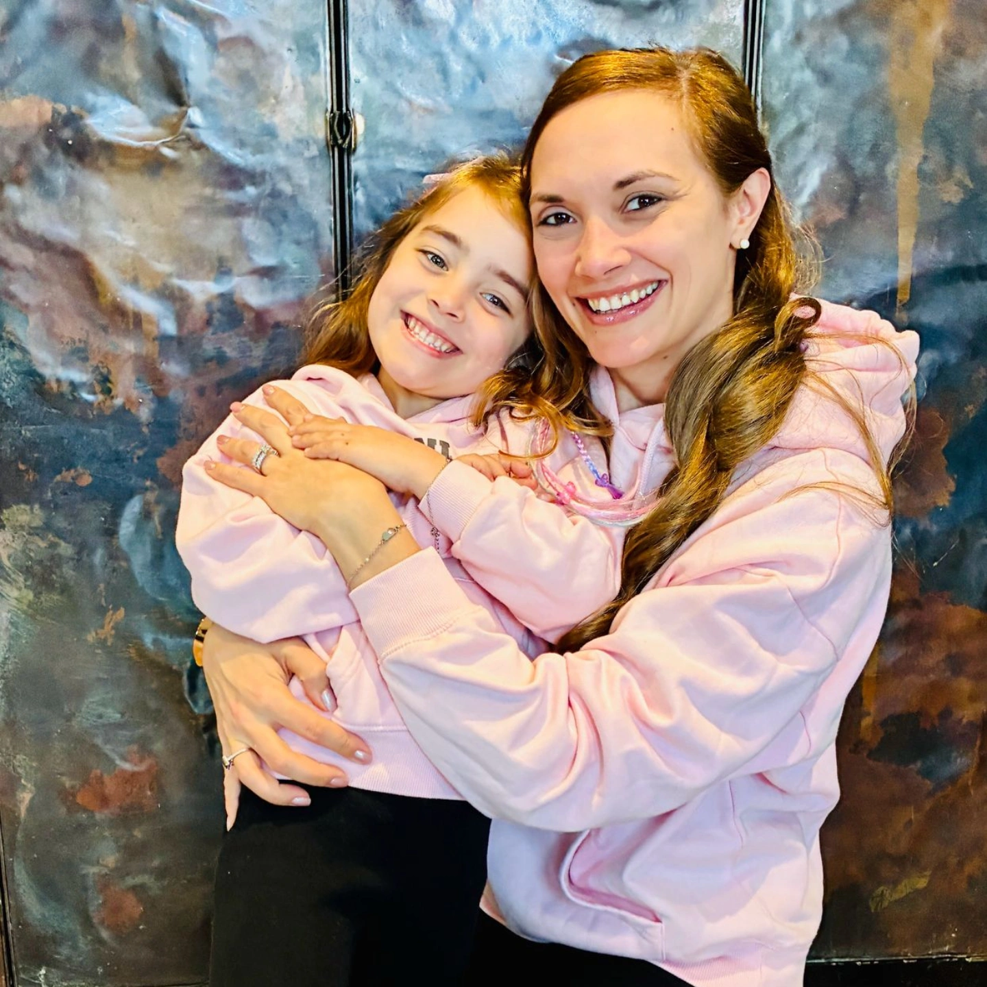 Cristina and Mia hugging in matching pink hoodies