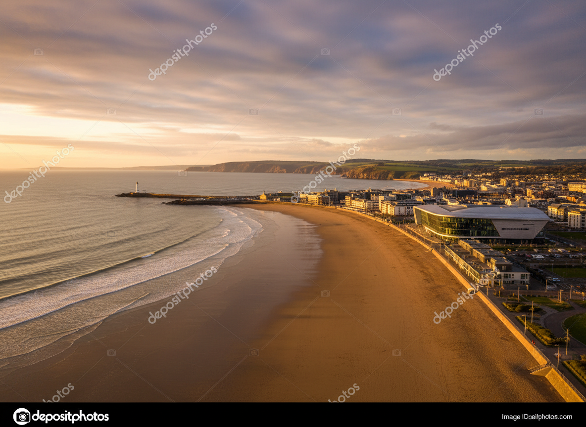 Swansea Bay waterfront at golden hour with the sweeping coastline, modern Swansea Arena, and Mumbles in the distance