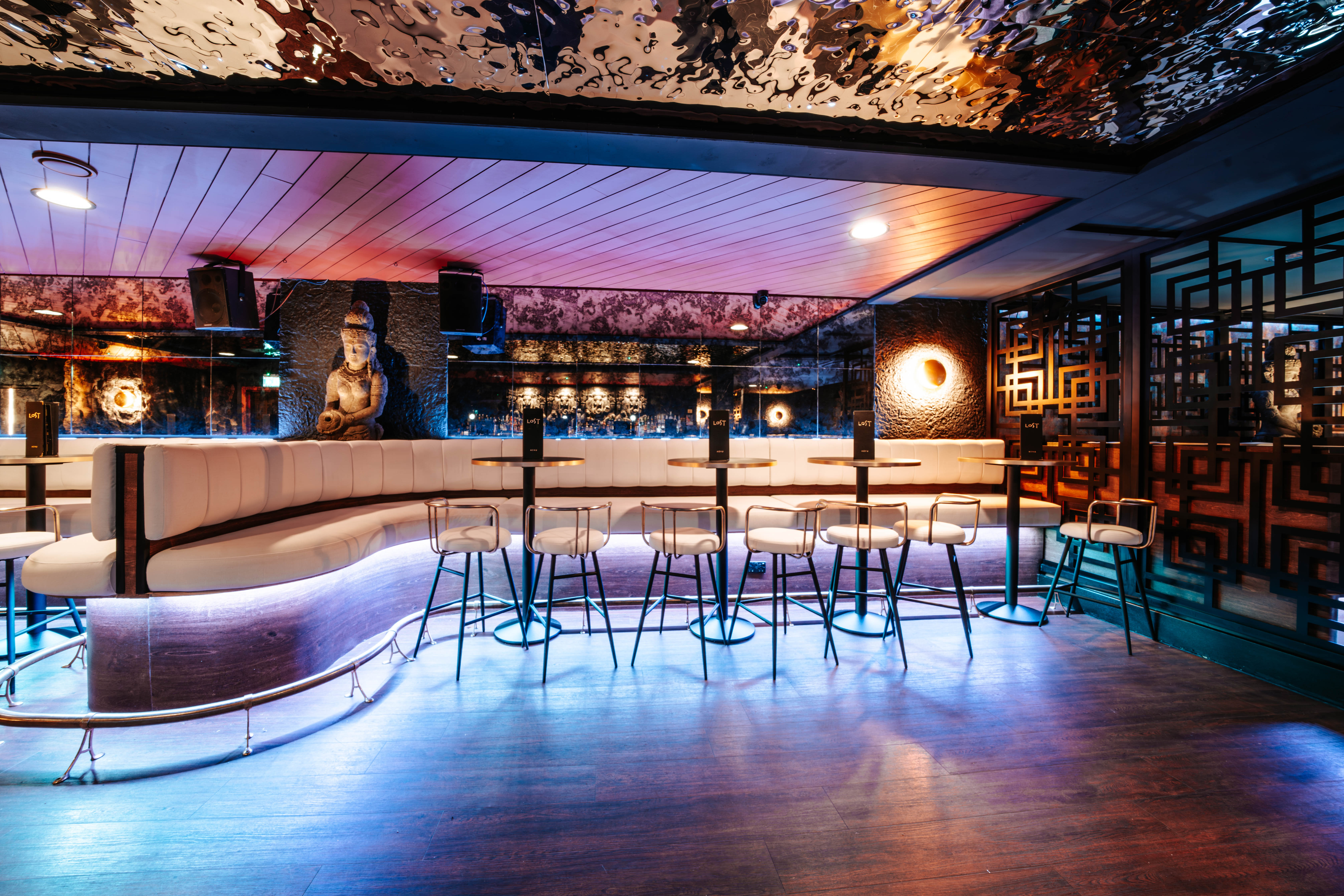 LOST Bournemouth main bar area with curved white leather booth seating, high stools, a carved stone statue and a reflective ceiling