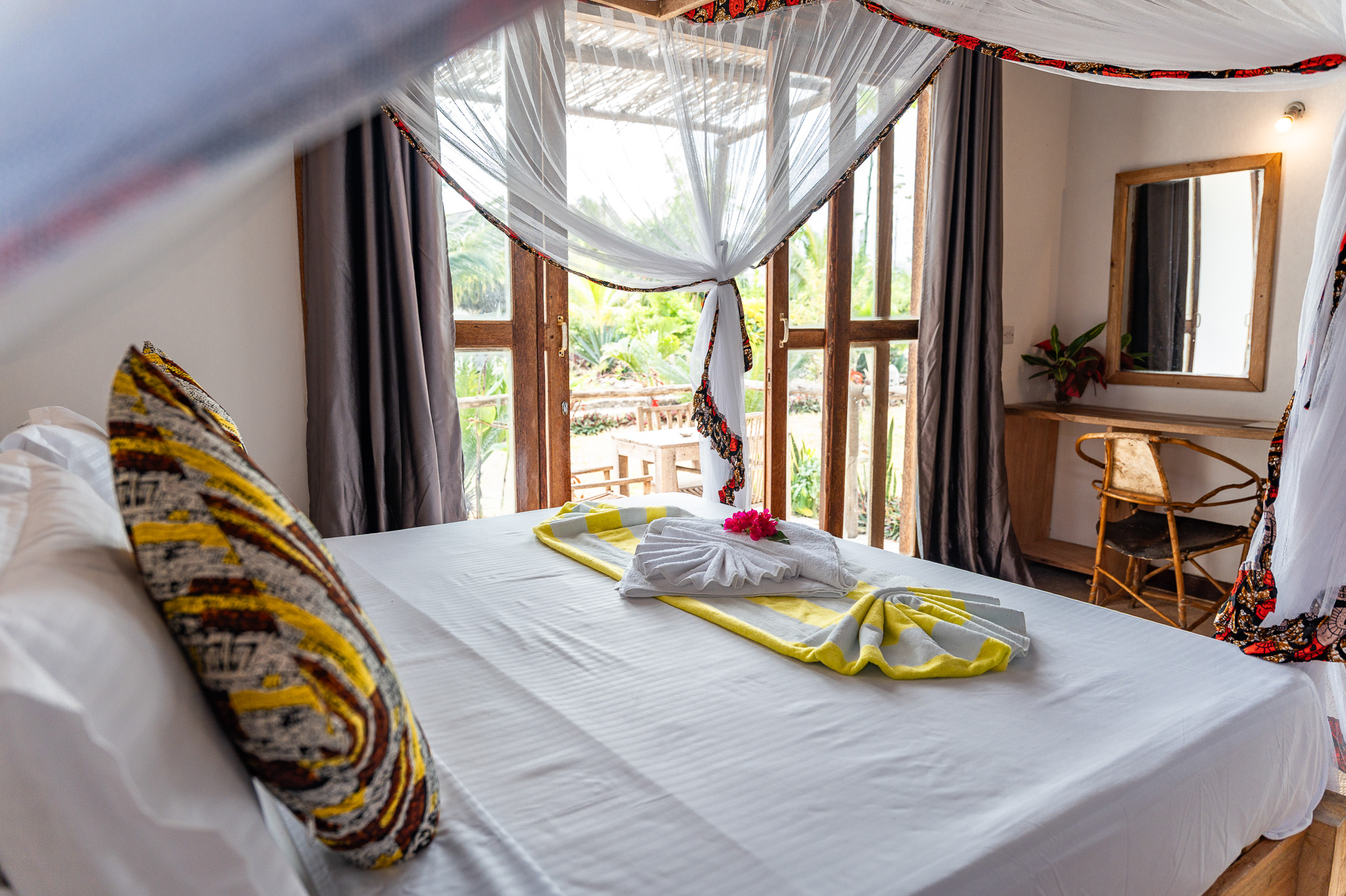 Double bed with mosquito net, kitenge pillows and flower decoration at Tunu Beach Zanzibar