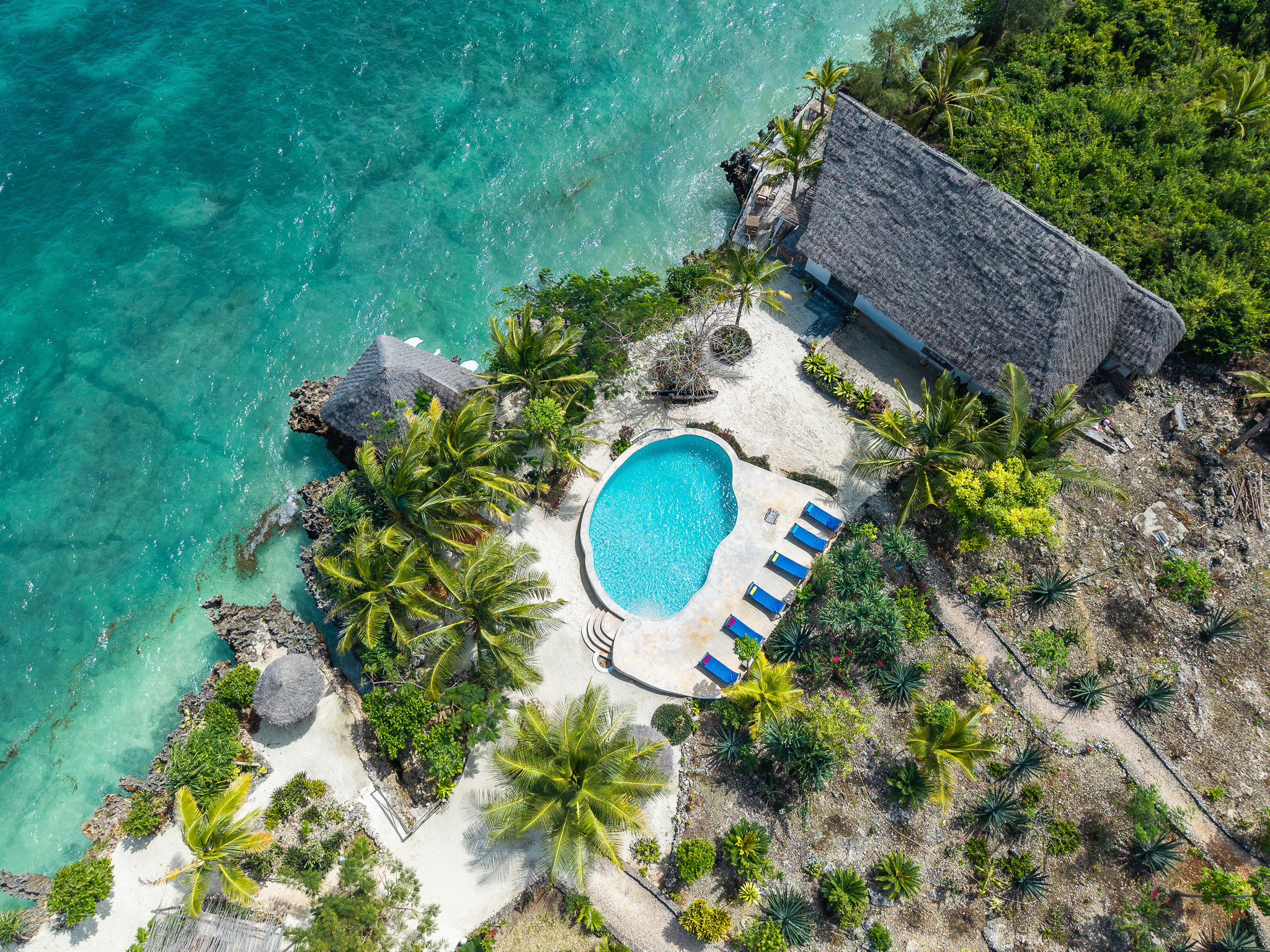 Aerial drone view of Tunu Beach Zanzibar resort — pool, bungalows, palm trees and turquoise ocean from above