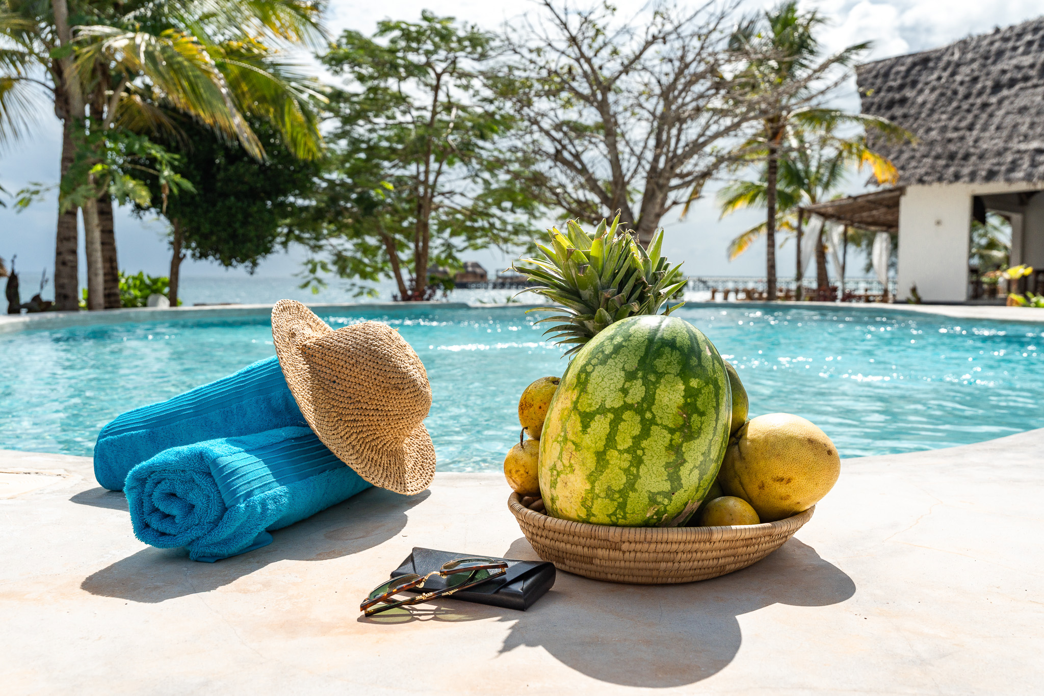 Poolside relaxation — tropical fruits, straw hat, sunglasses and turquoise water with ocean view