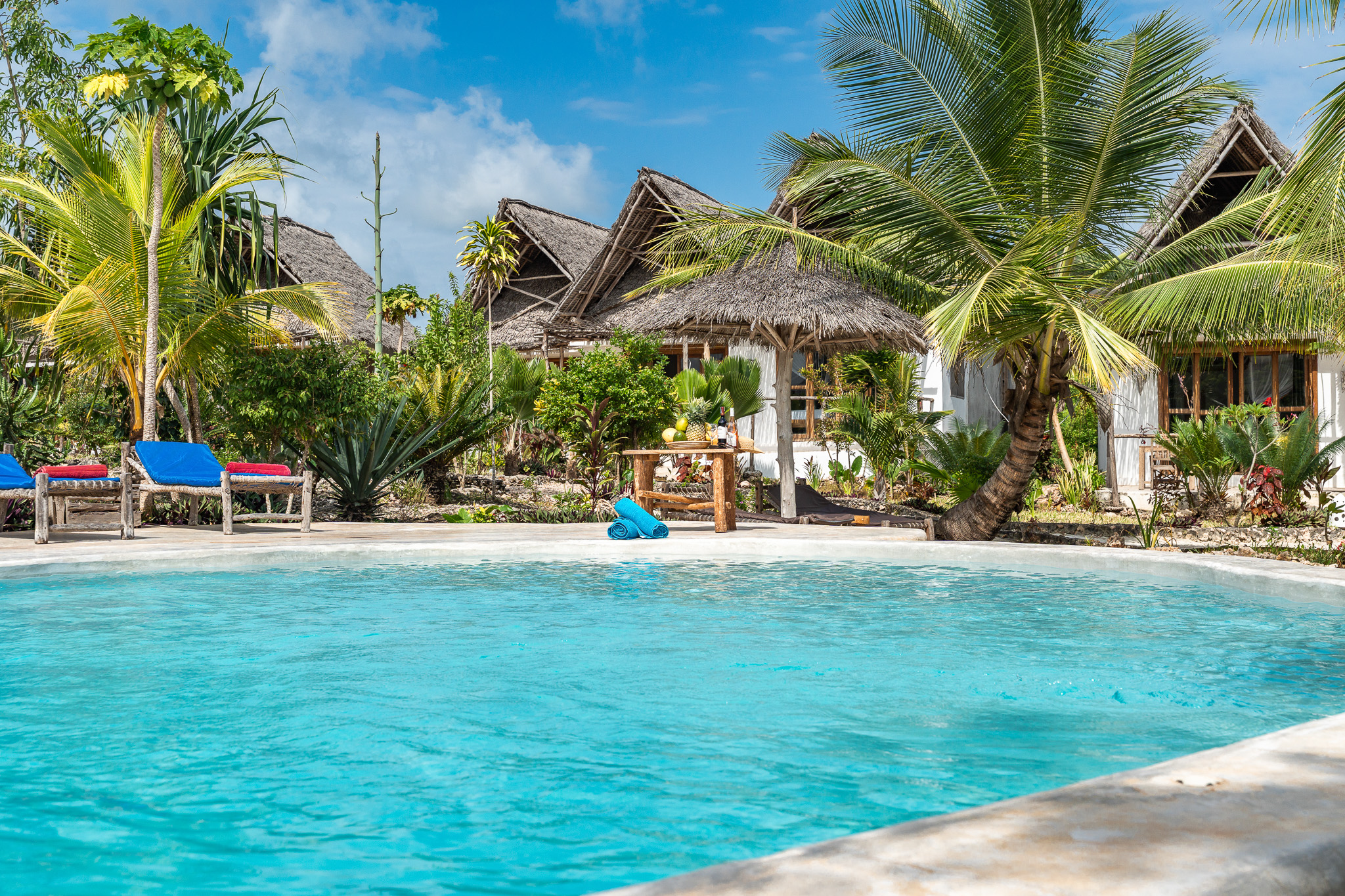 Swimming pool with makuti-roof bungalows, palm trees and sun loungers at Tunu Beach Zanzibar