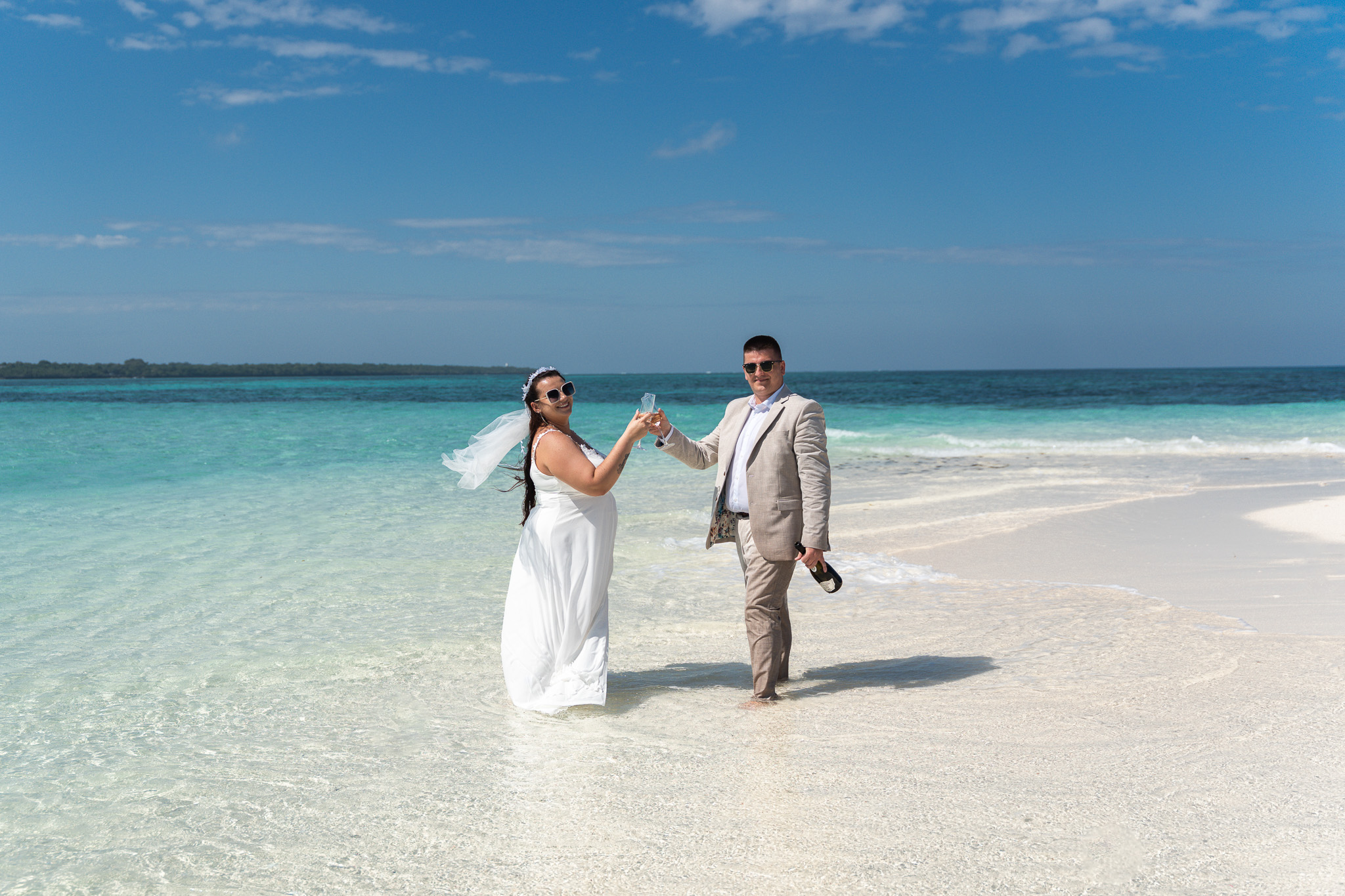 Wedding couple toasting champagne on sandbank in Zanzibar with turquoise water