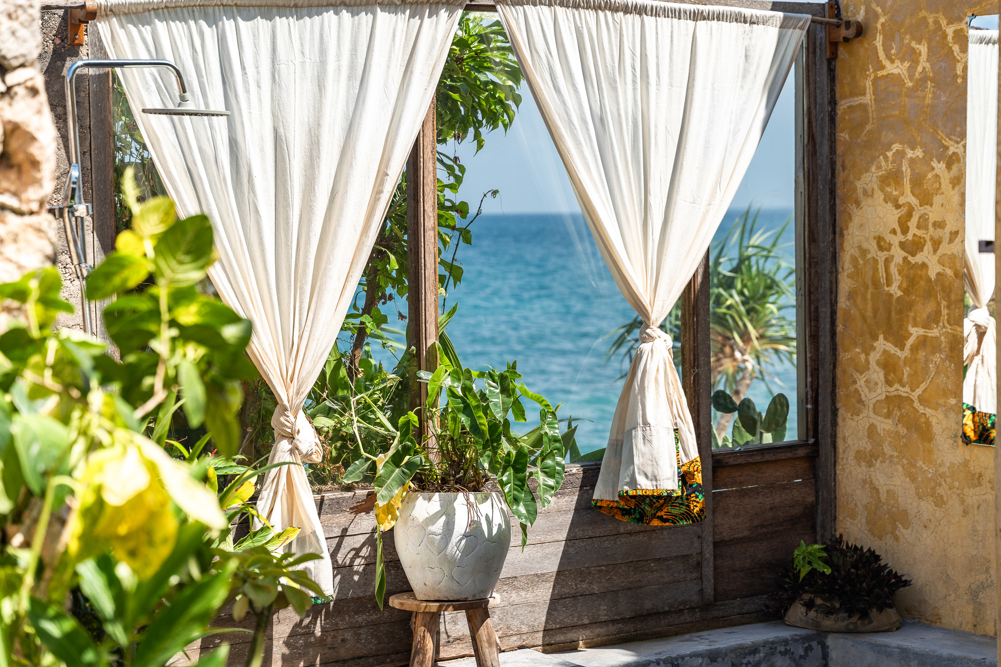 Outdoor bathroom detail — white curtains, ocean breeze, natural stone walls