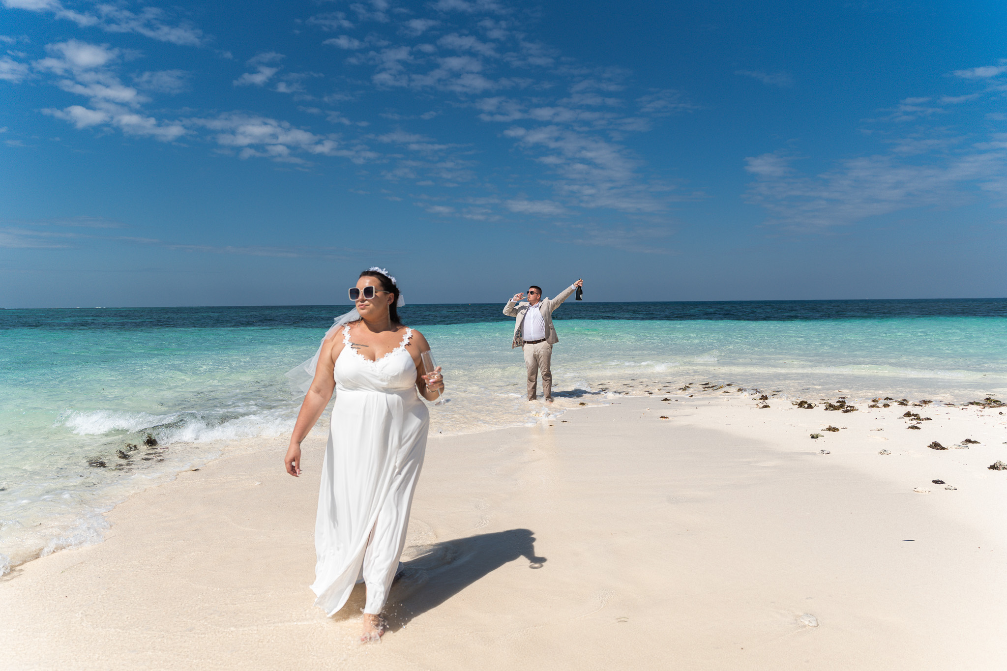 Bride walking on sandbank beach with groom celebrating in background - Zanzibar
