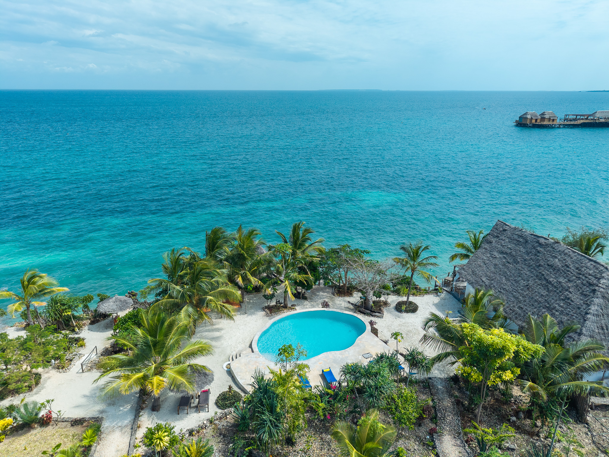 Aerial drone view of Tunu Beach Zanzibar — beachfront pool surrounded by palm trees and turquoise Indian Ocean