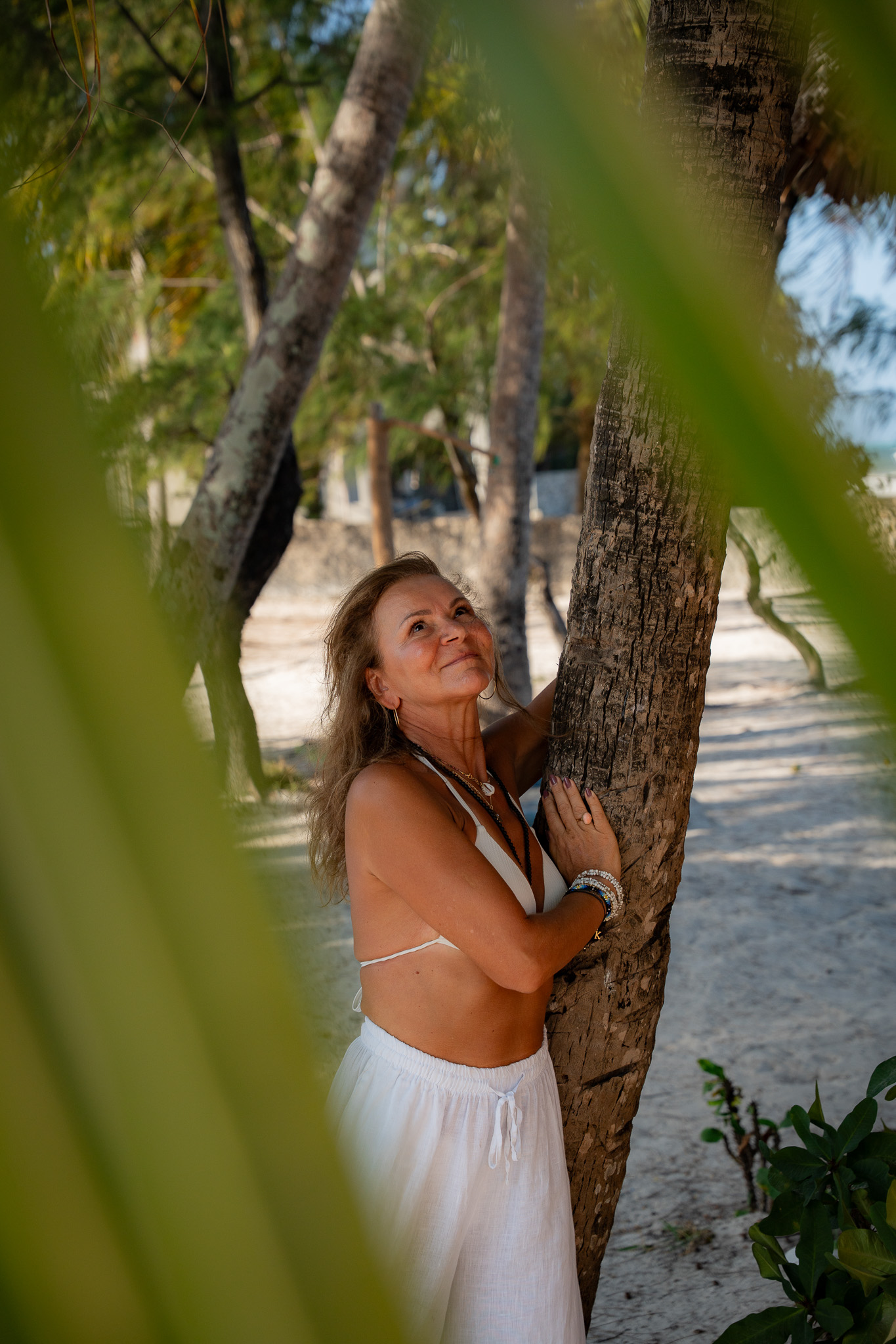 Woman in white dress embracing a palm tree on Zanzibar beach