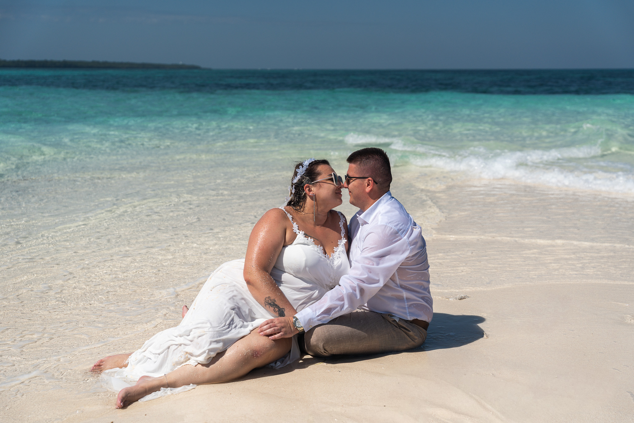 Intimate couple sitting on sandbank beach kissing with turquoise ocean - Zanzibar