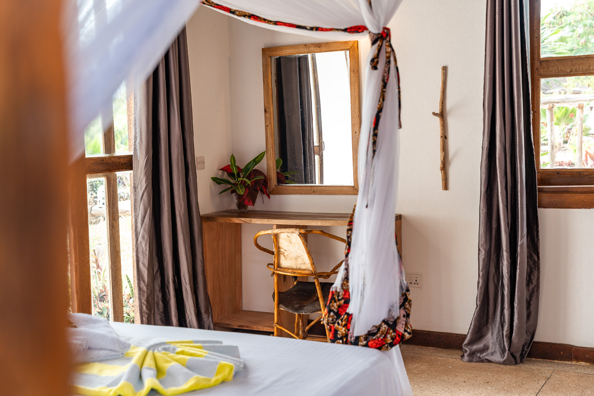 Room interior detail — wooden vanity, mirror, rattan chair and tropical plant