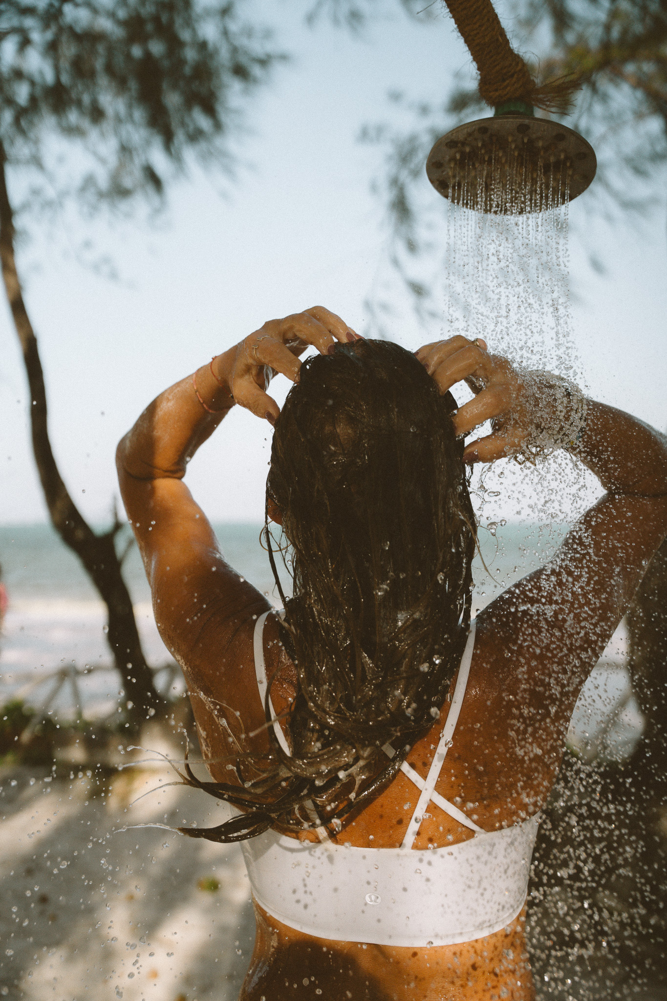 Woman rinsing hair under outdoor beach shower in Zanzibar