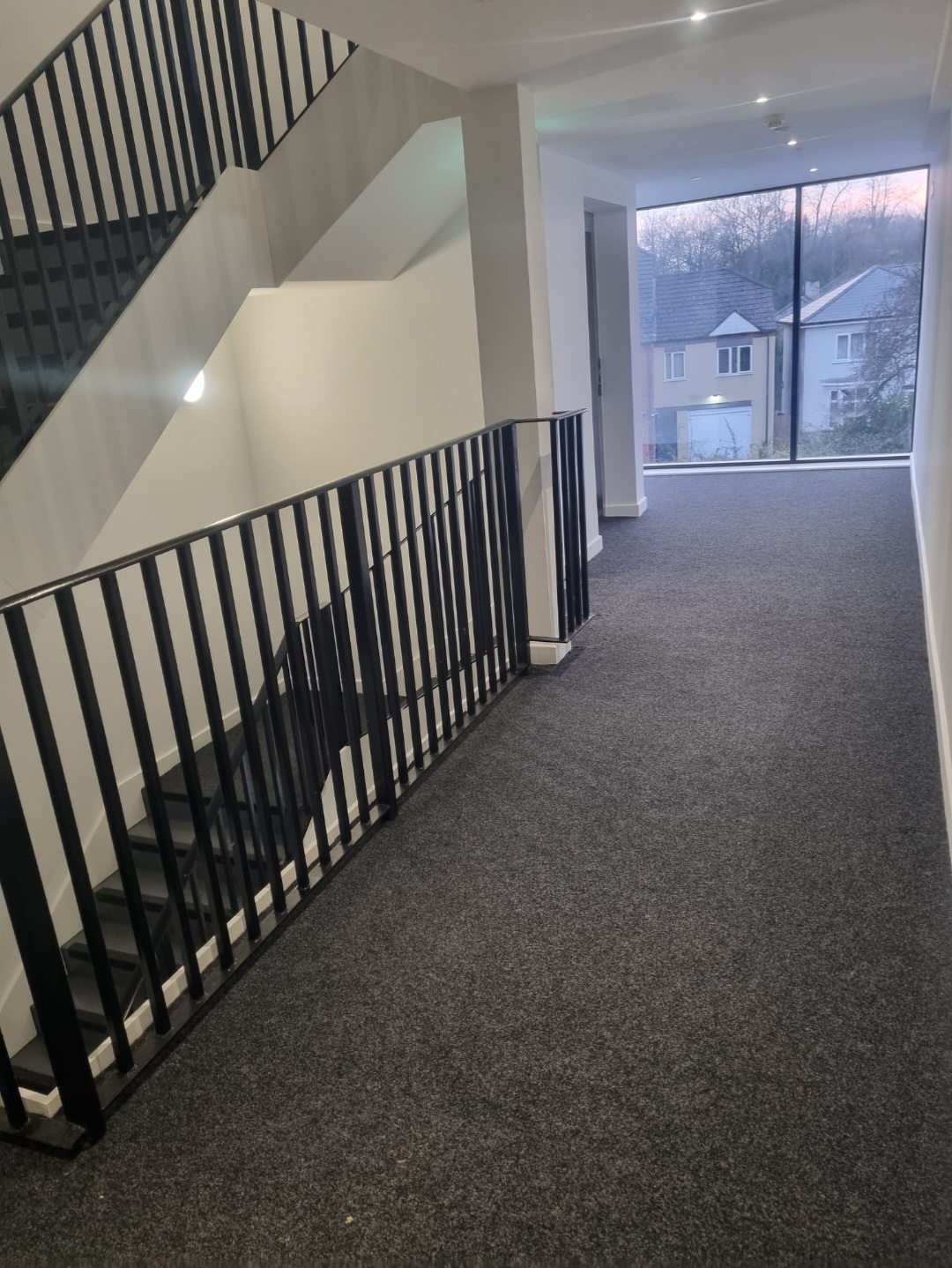 Modern hallway with dark carpet and black staircase balustrade