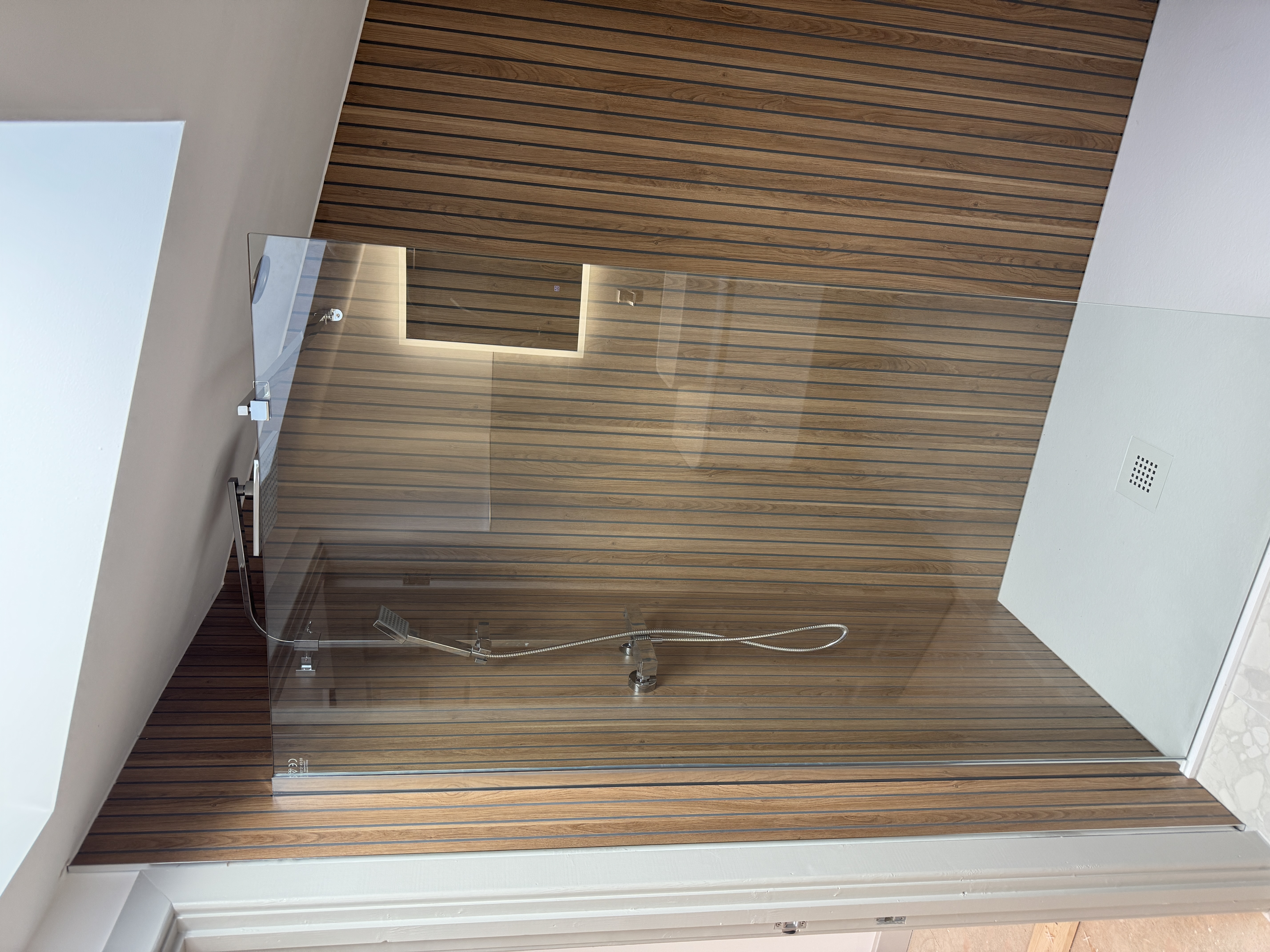 Shower enclosure with wooden slats and sloped ceiling