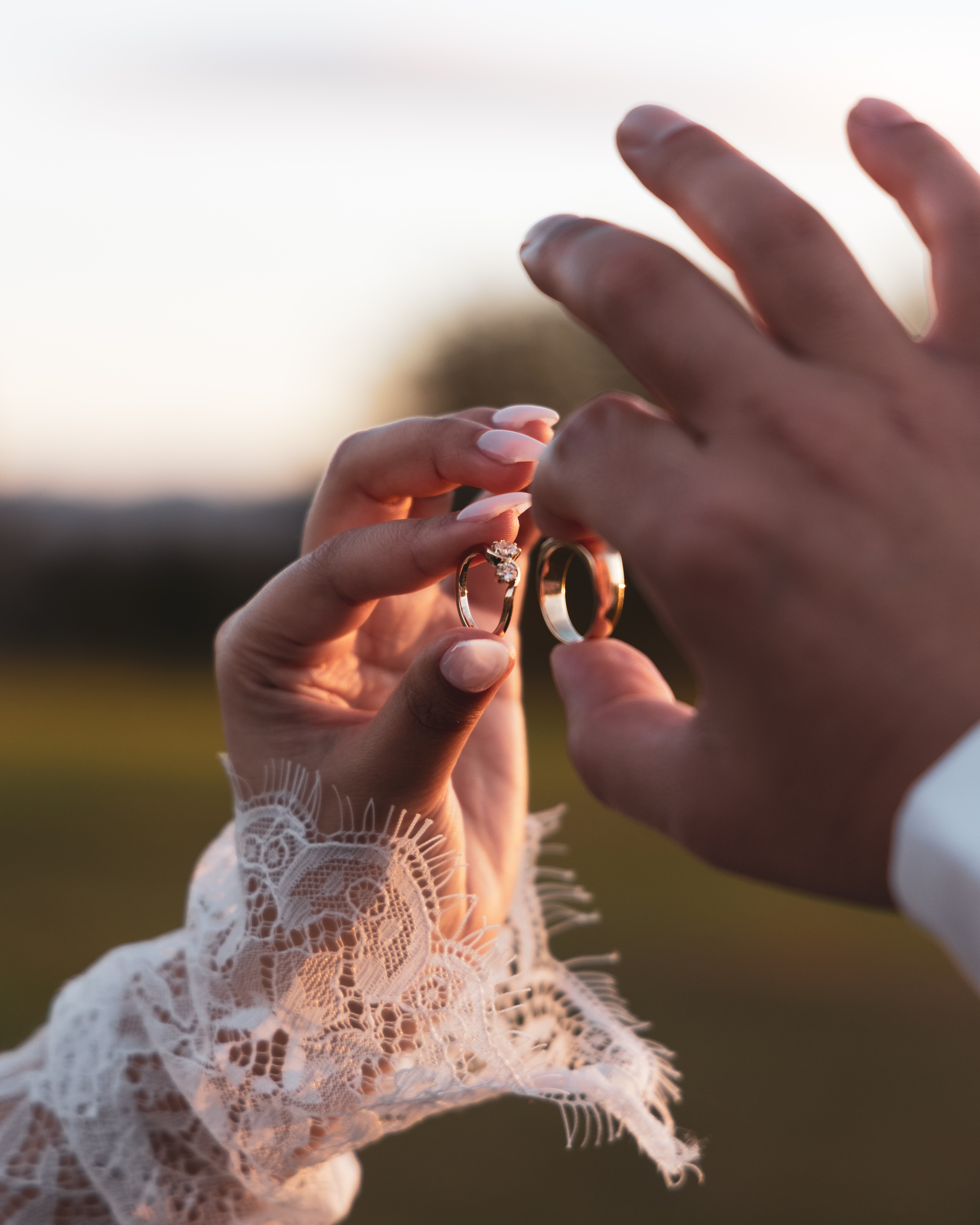 Bride and groom holding wedding rings at golden hour