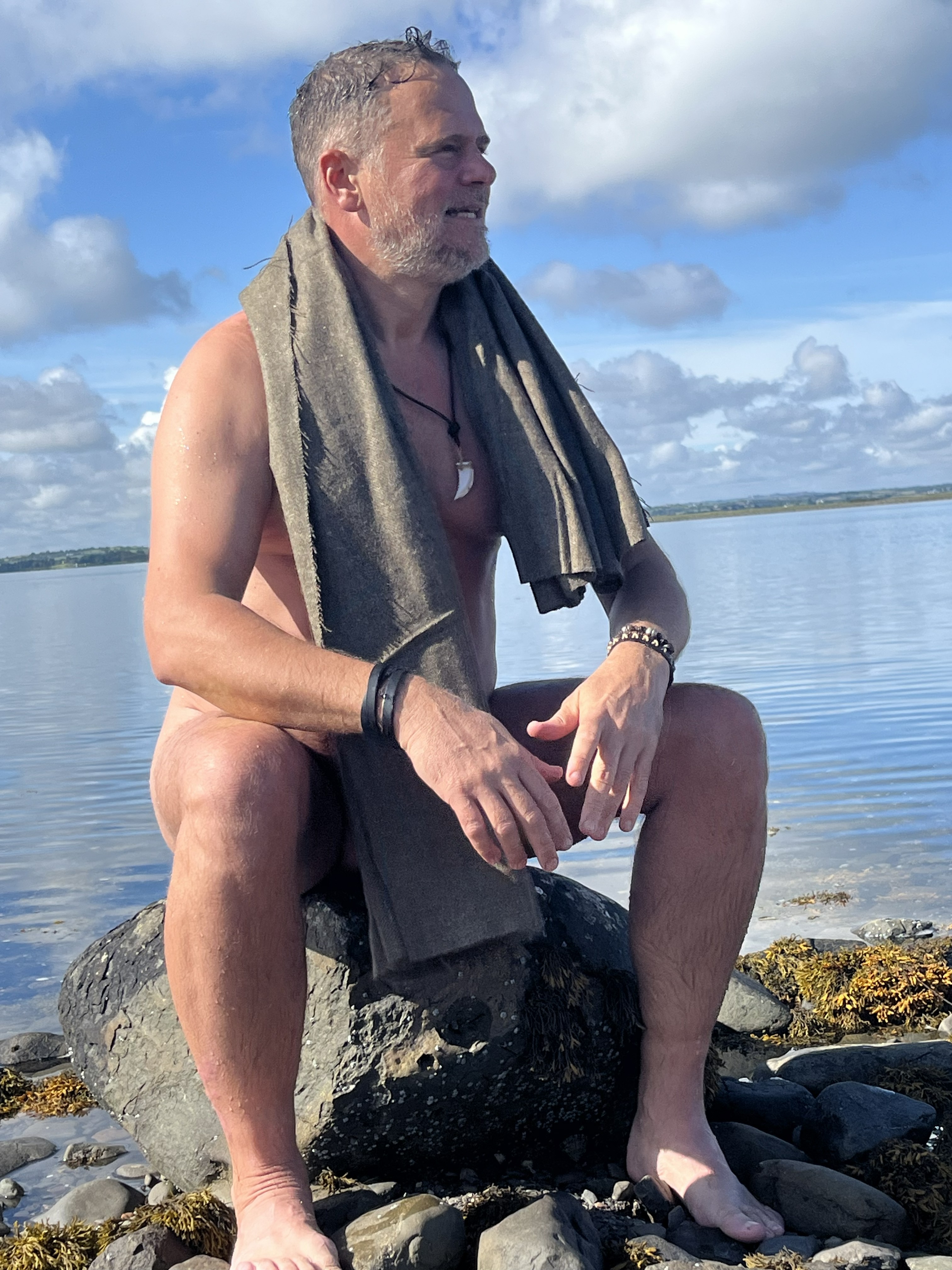 Garreth sitting on rocks by the water after a swim