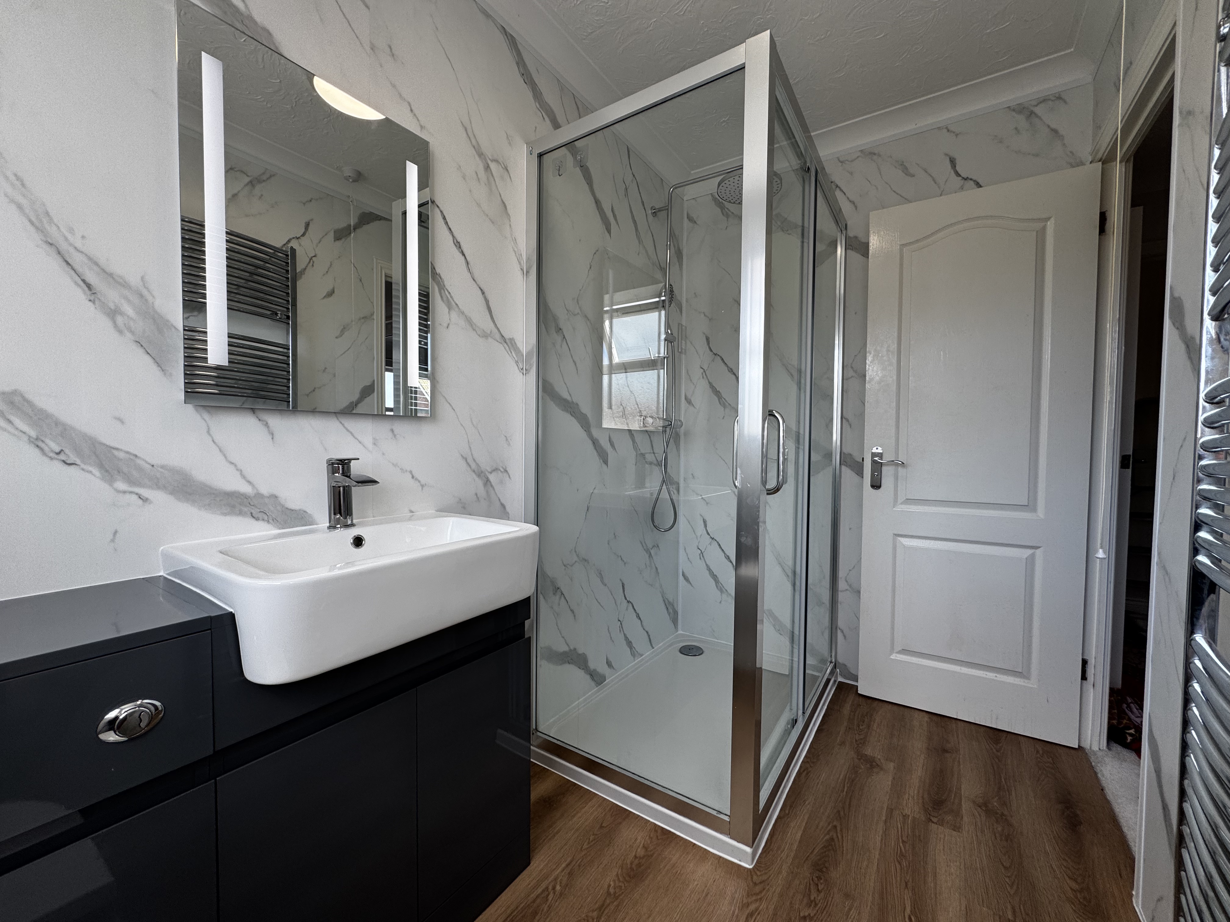 Stylish shower room with marble-effect walls, dark vanity unit, and glass shower enclosure