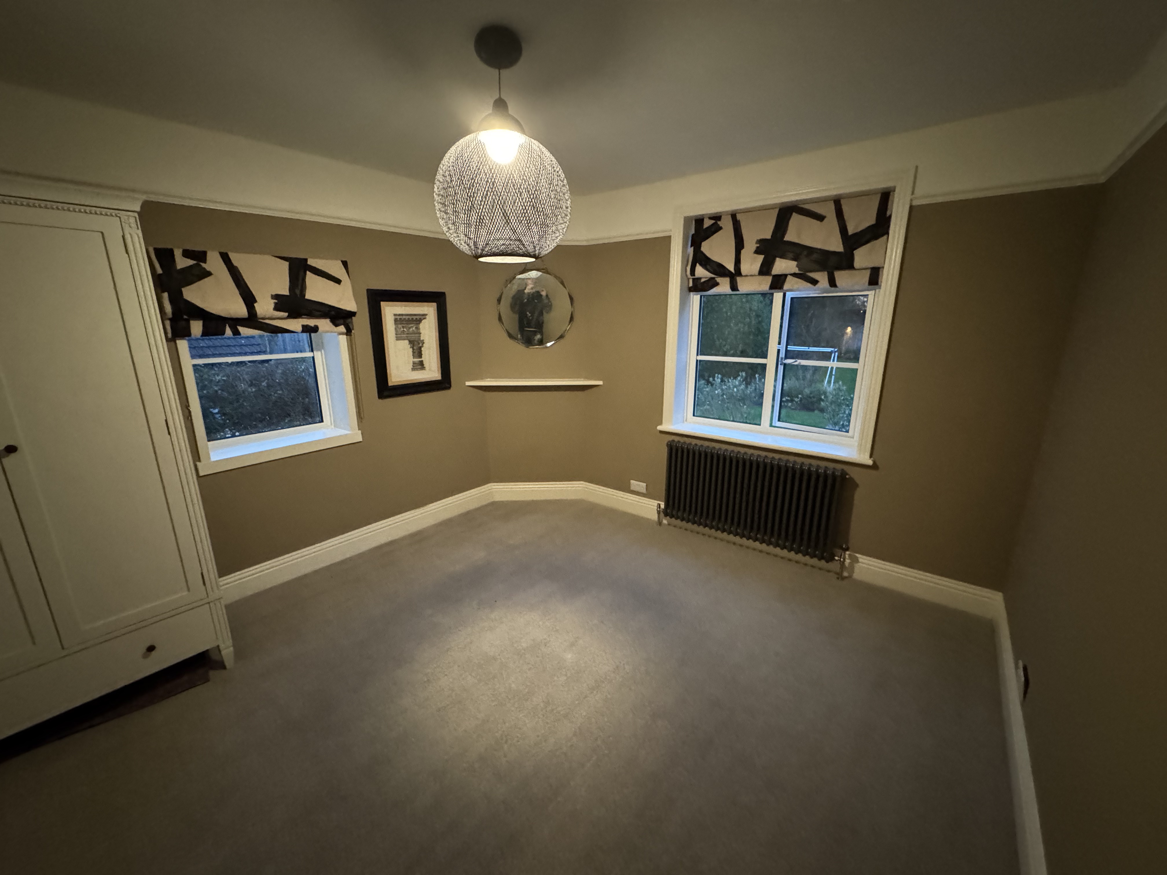 Elegantly decorated bedroom with warm taupe walls, patterned roman blinds, and statement pendant light