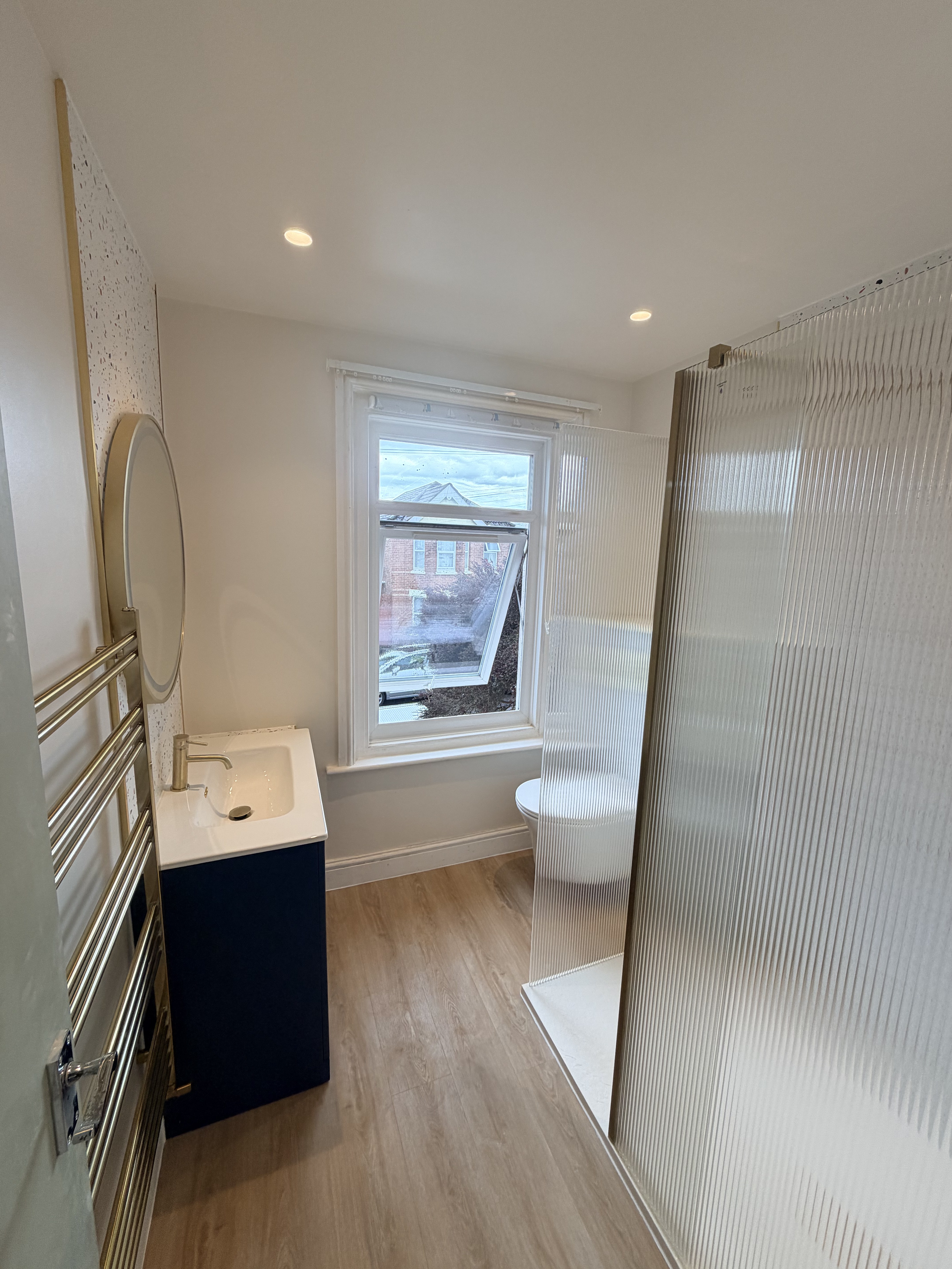 Bathroom overview showing shower enclosure, wall-hung WC and navy vanity — Charminster bedroom conversion
