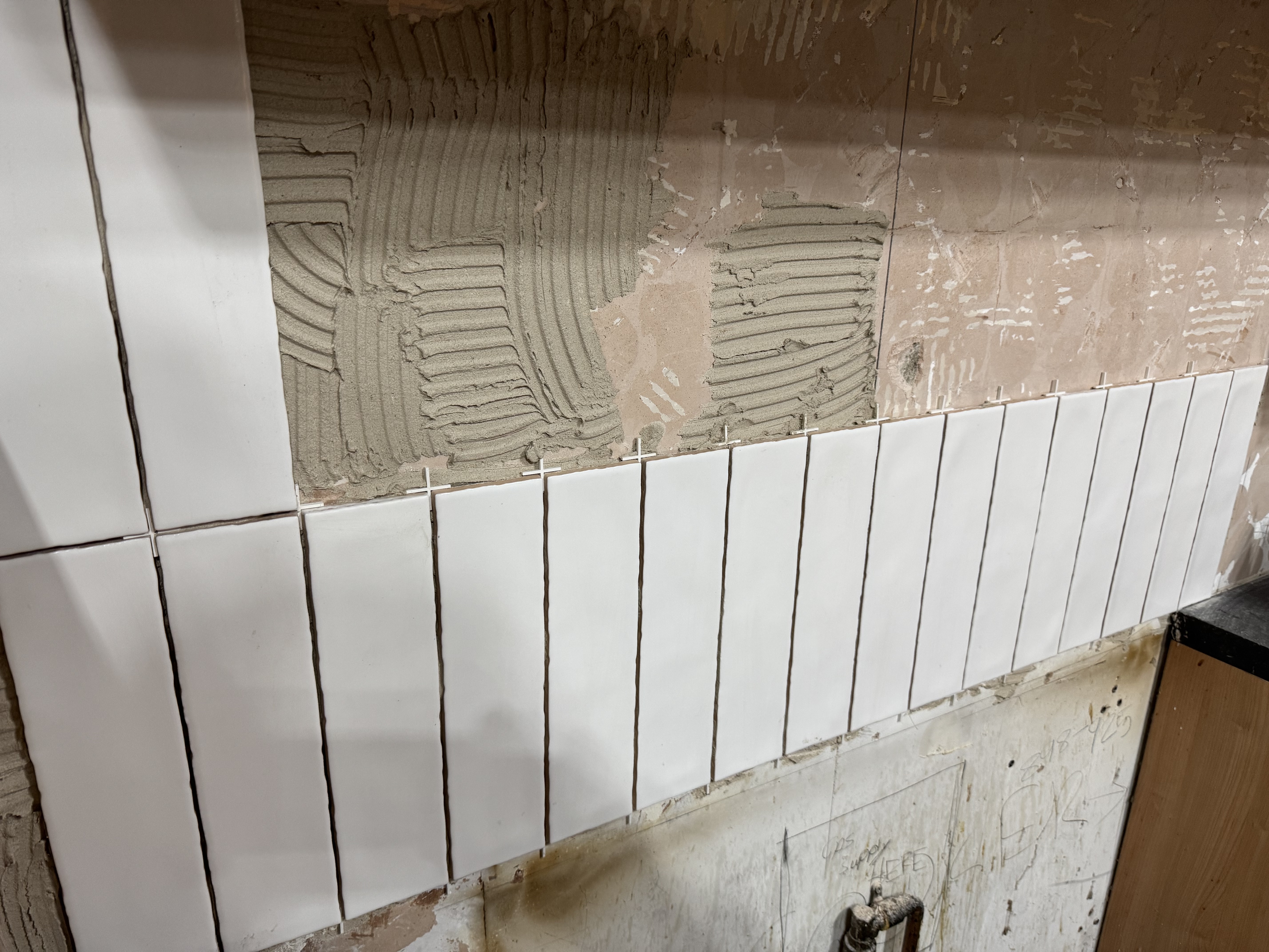 Porcelain white tile backsplash installation in progress with adhesive and spacers