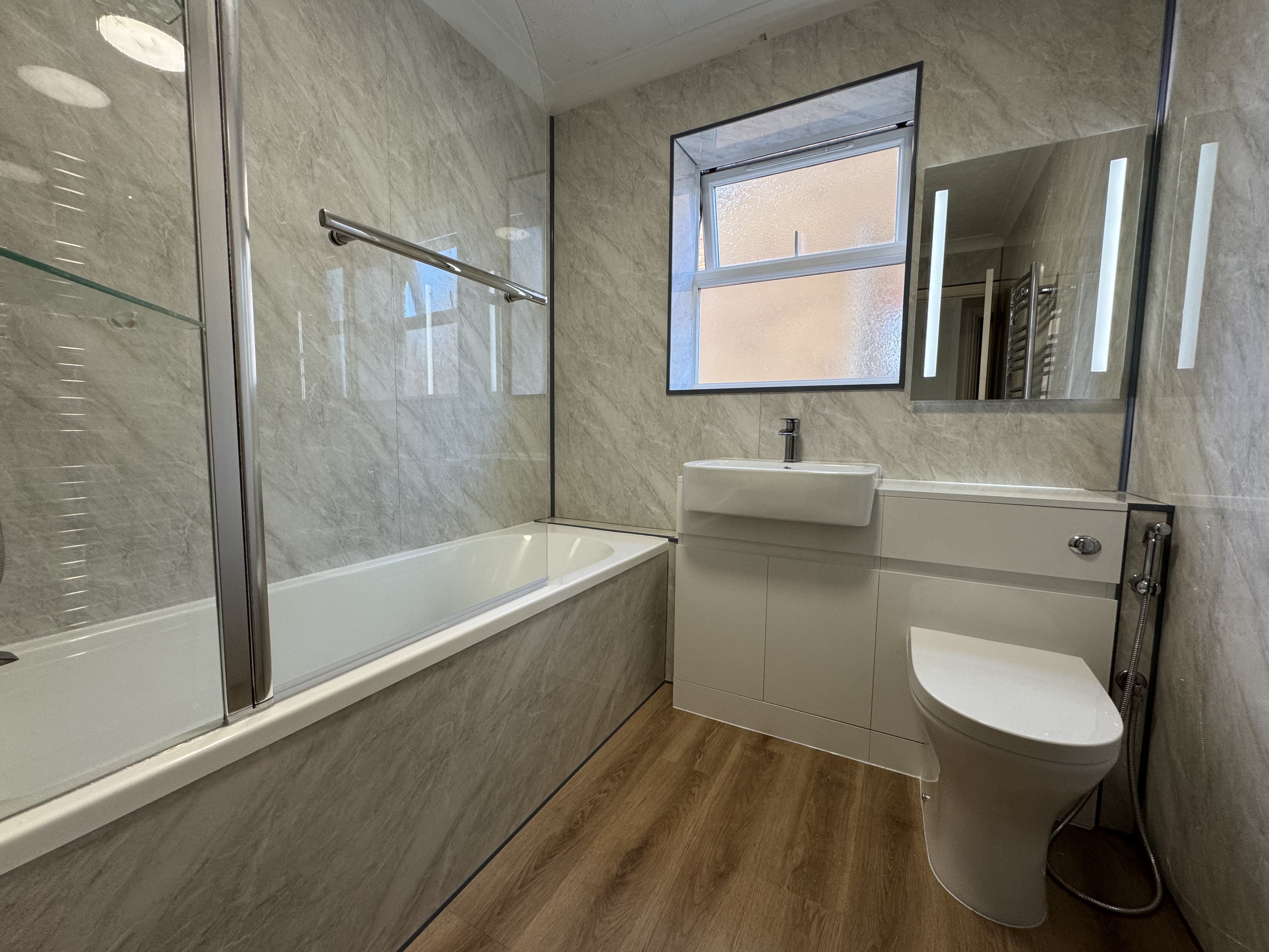 Modern bathroom with marble-effect wall panels, bath with glass shower screen, and oak-effect flooring