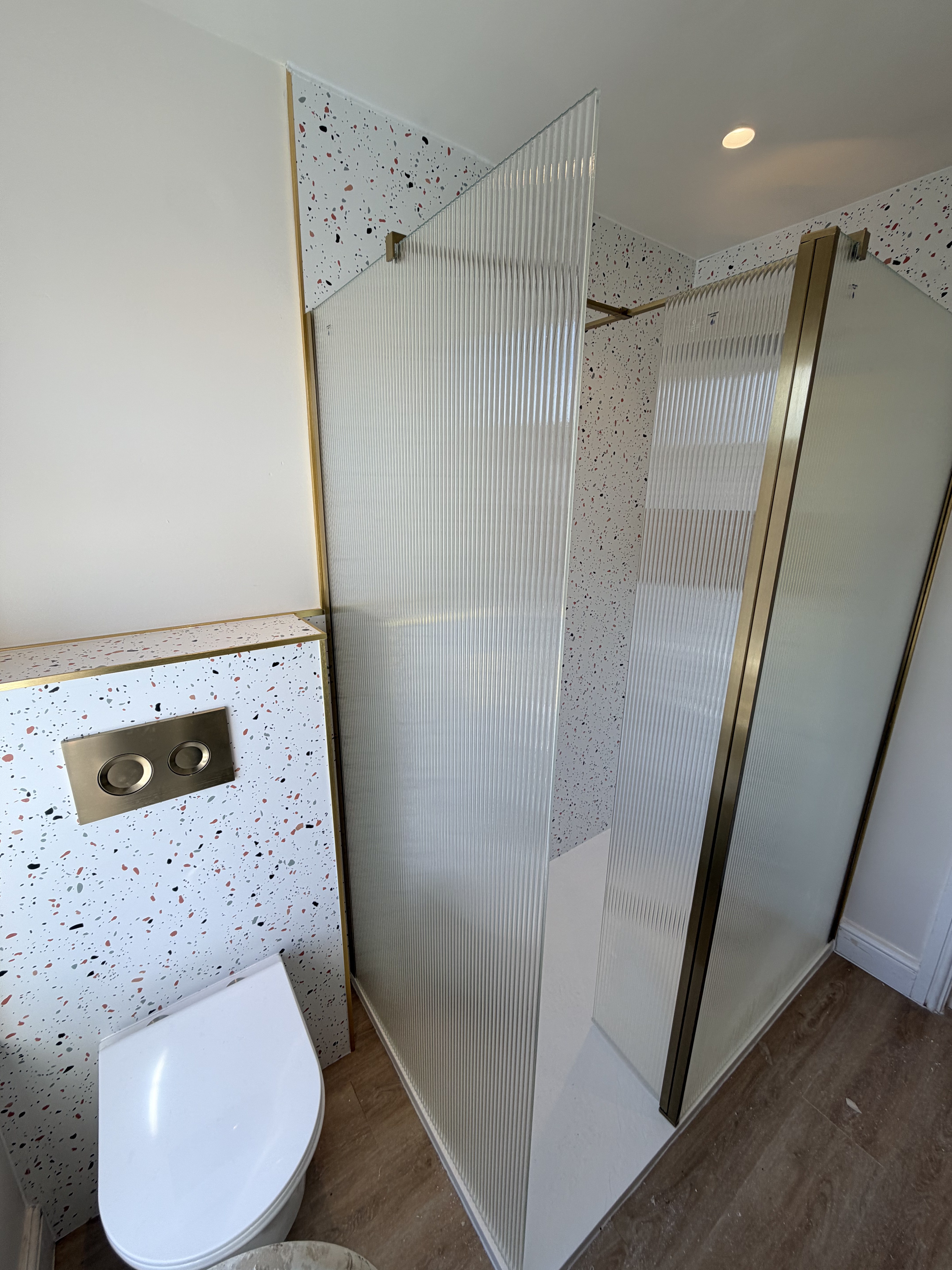 Full bathroom view — reeded glass shower screen with brass frame, navy vanity and oak LVT flooring — Charminster