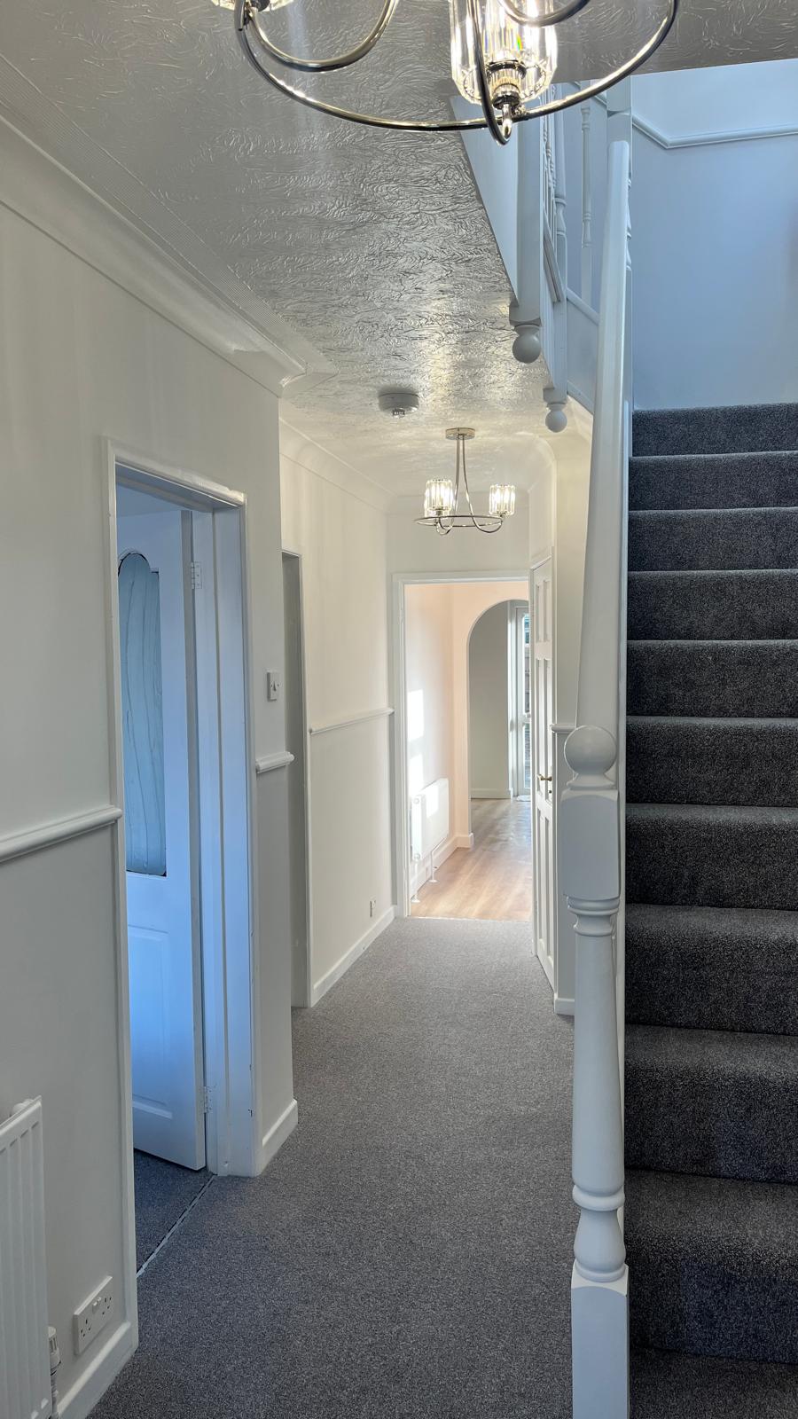 Freshly painted hallway and staircase in crisp white with new carpet and elegant lighting