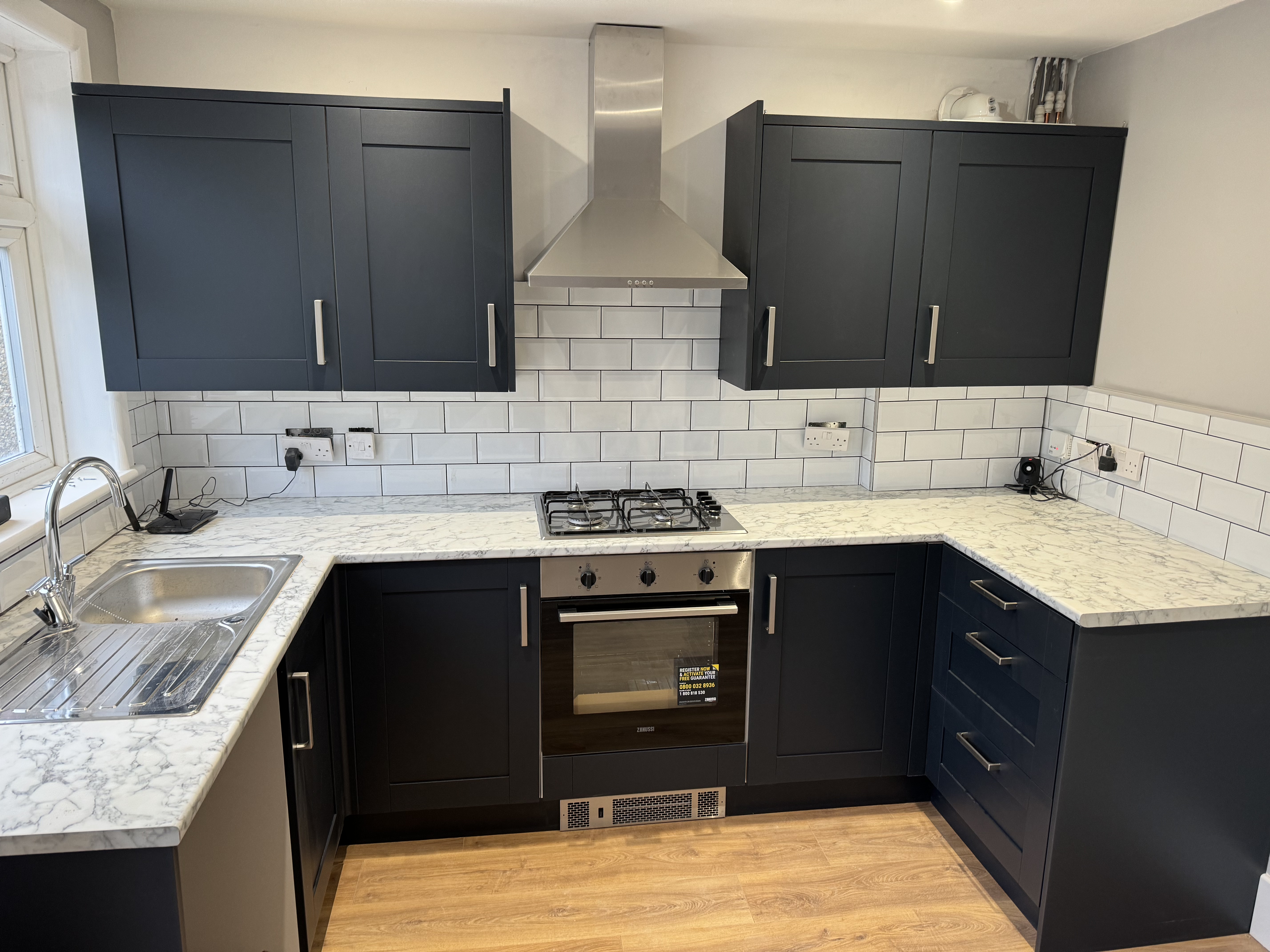 Dark blue kitchen with marble-effect worktops, subway tile splashback and stainless steel hood