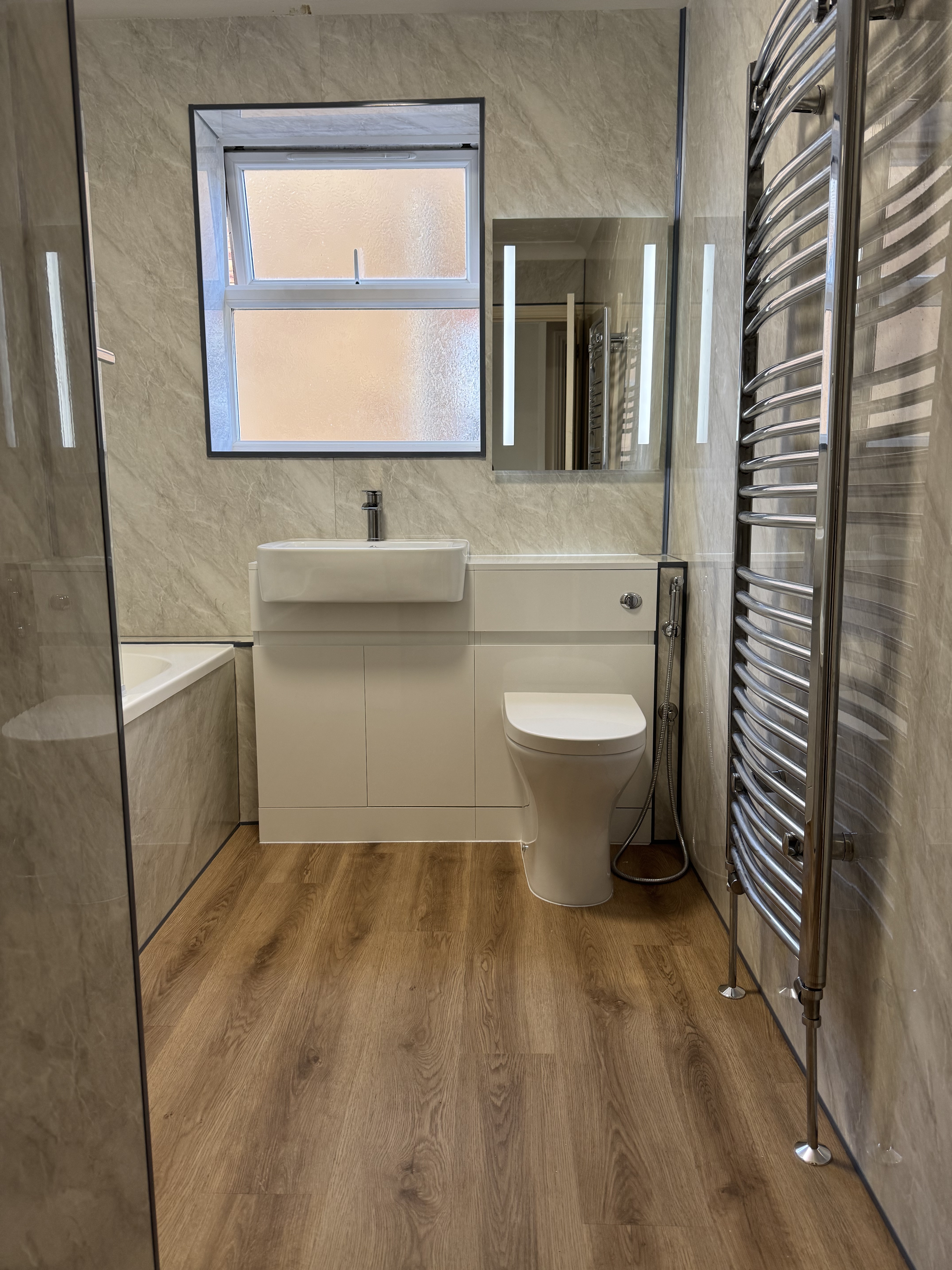 Luxury vinyl tile bathroom flooring with marble-effect wall tiles and heated towel rail