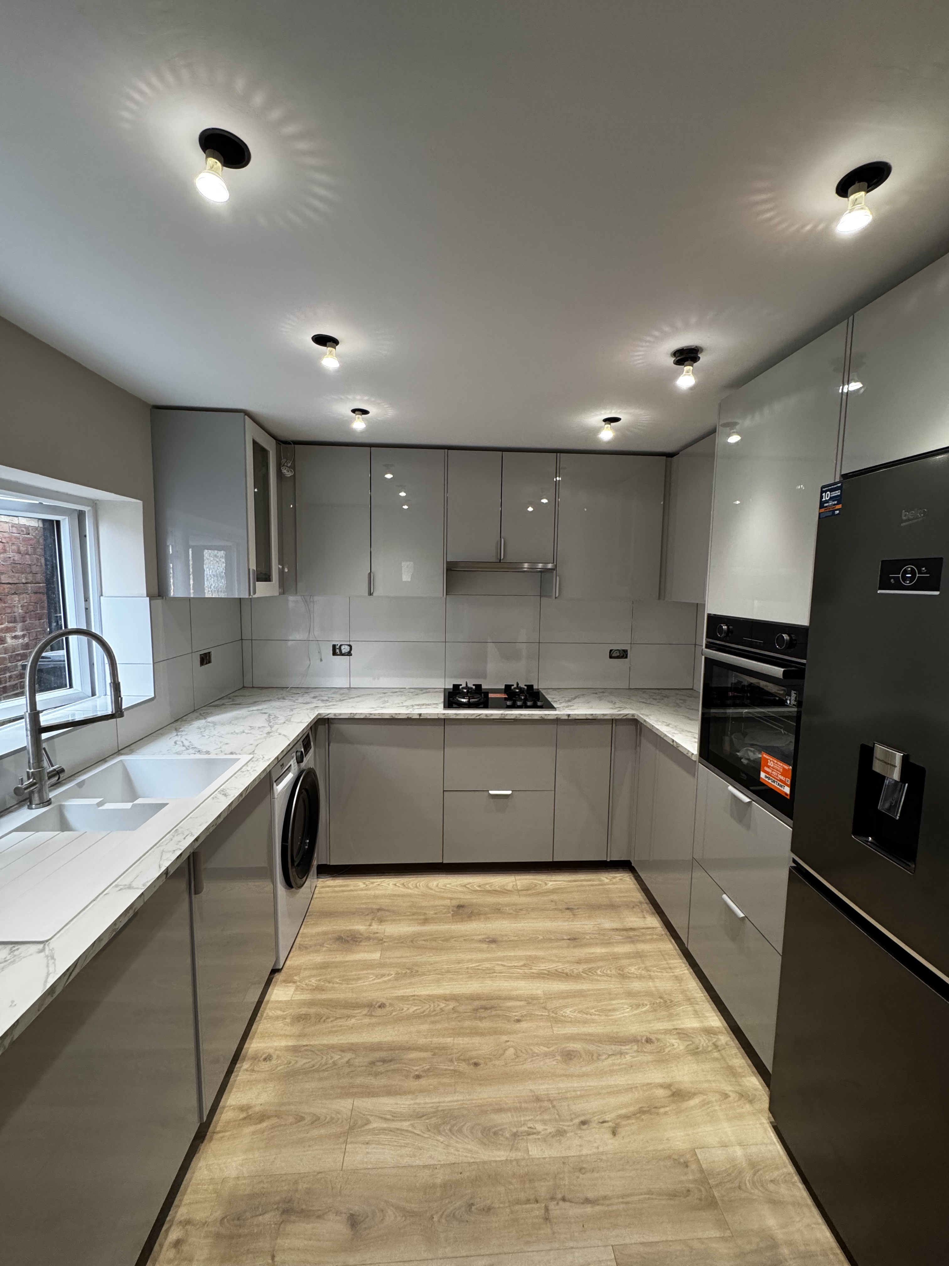 Modern grey gloss kitchen with marble-effect worktops, integrated appliances and oak flooring